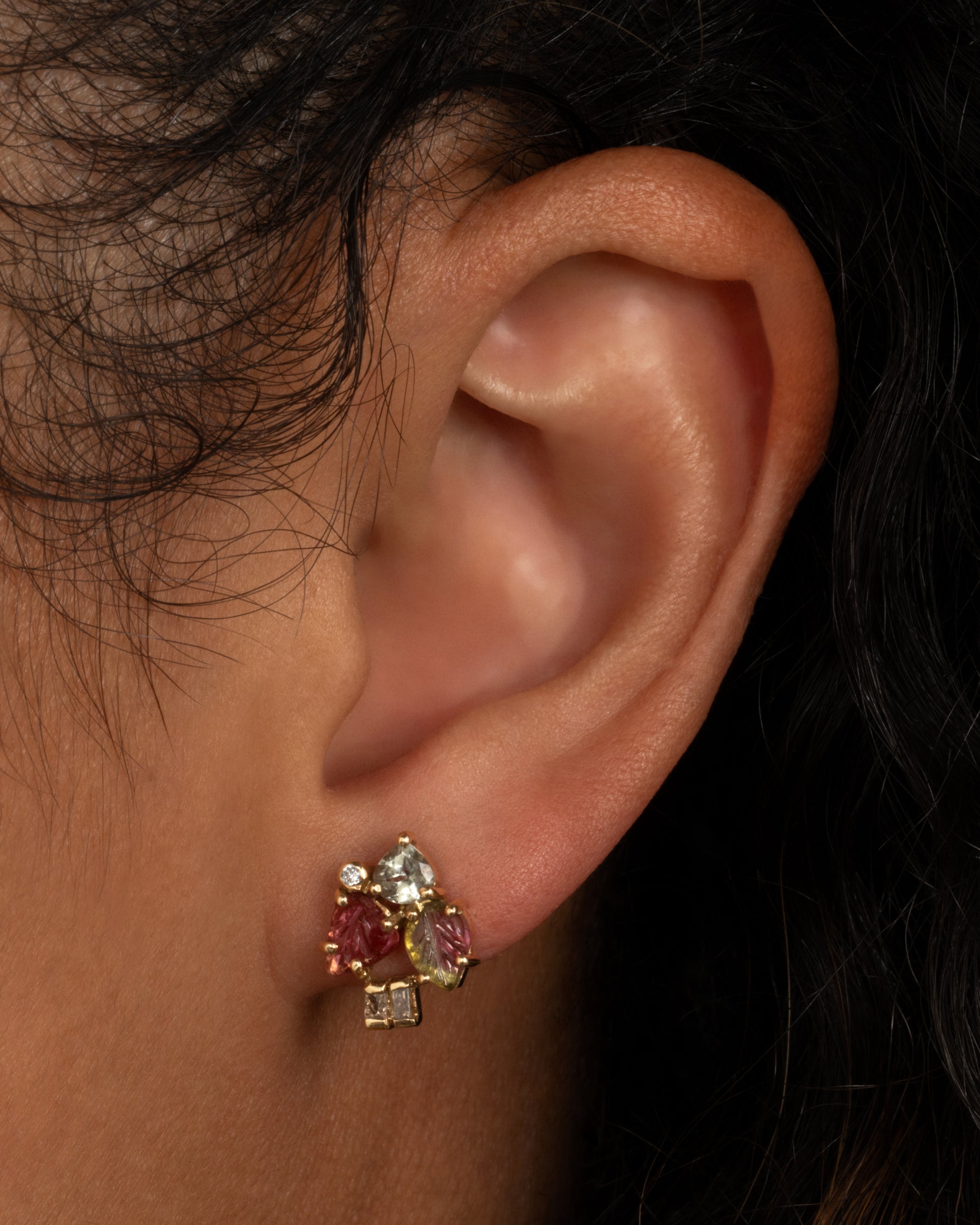 A yellow gold stud earring with botanical carved tourmalines and diamond accents. Shown worn in an ear.