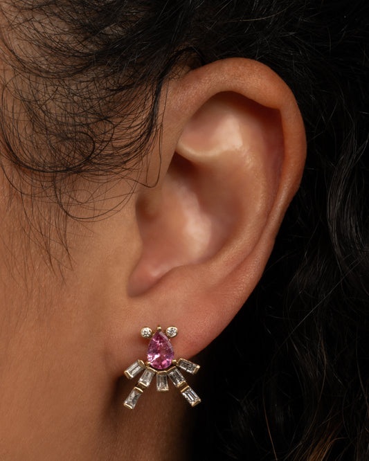 A yellow gold earring shaped like an abstract octopus made of pink sapphires and diamonds. Shown worn in an ear.