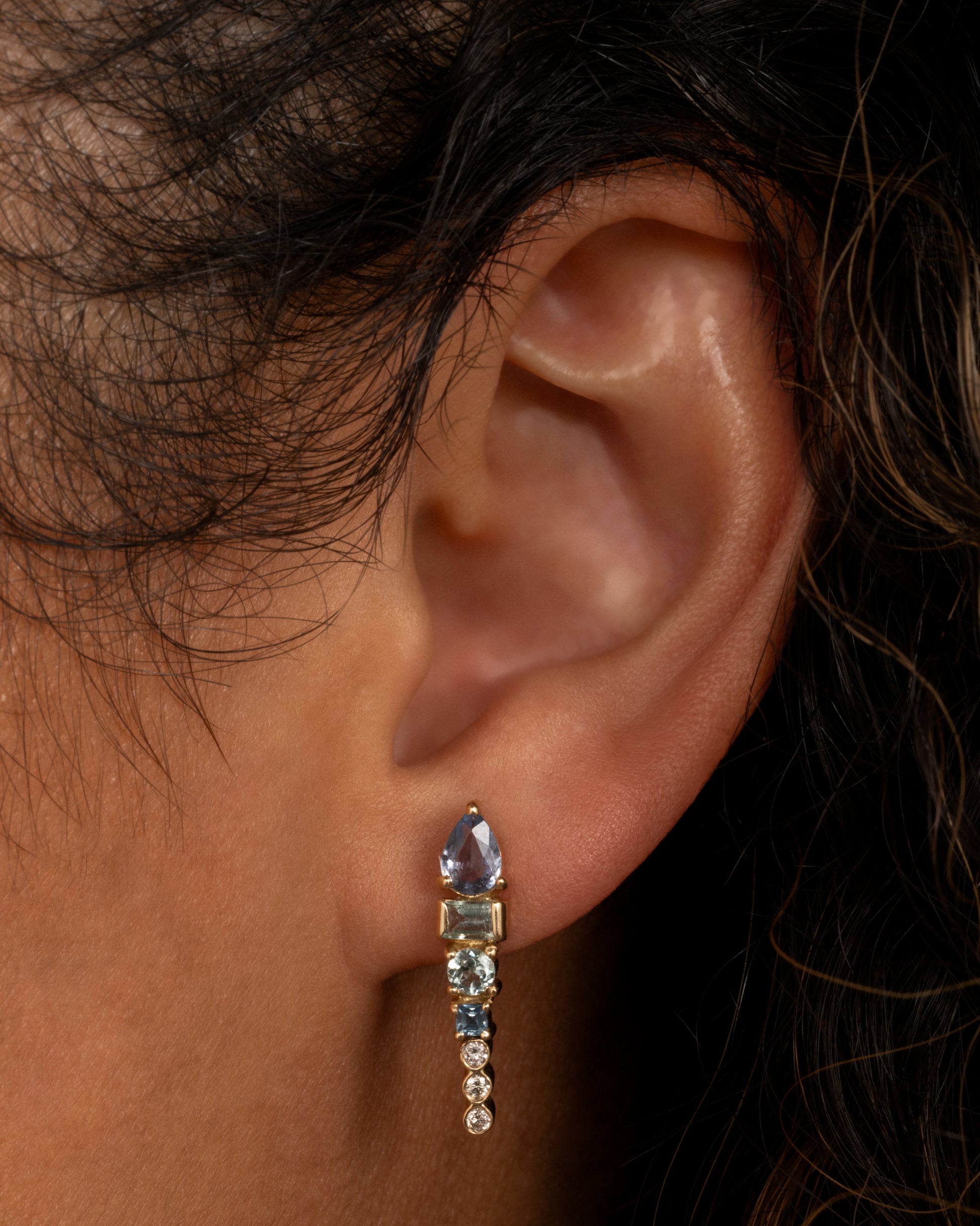 A long stud earring with an aquamarine, tanzanite, apatite, and three round diamonds stacked. Shown from the front on a person.