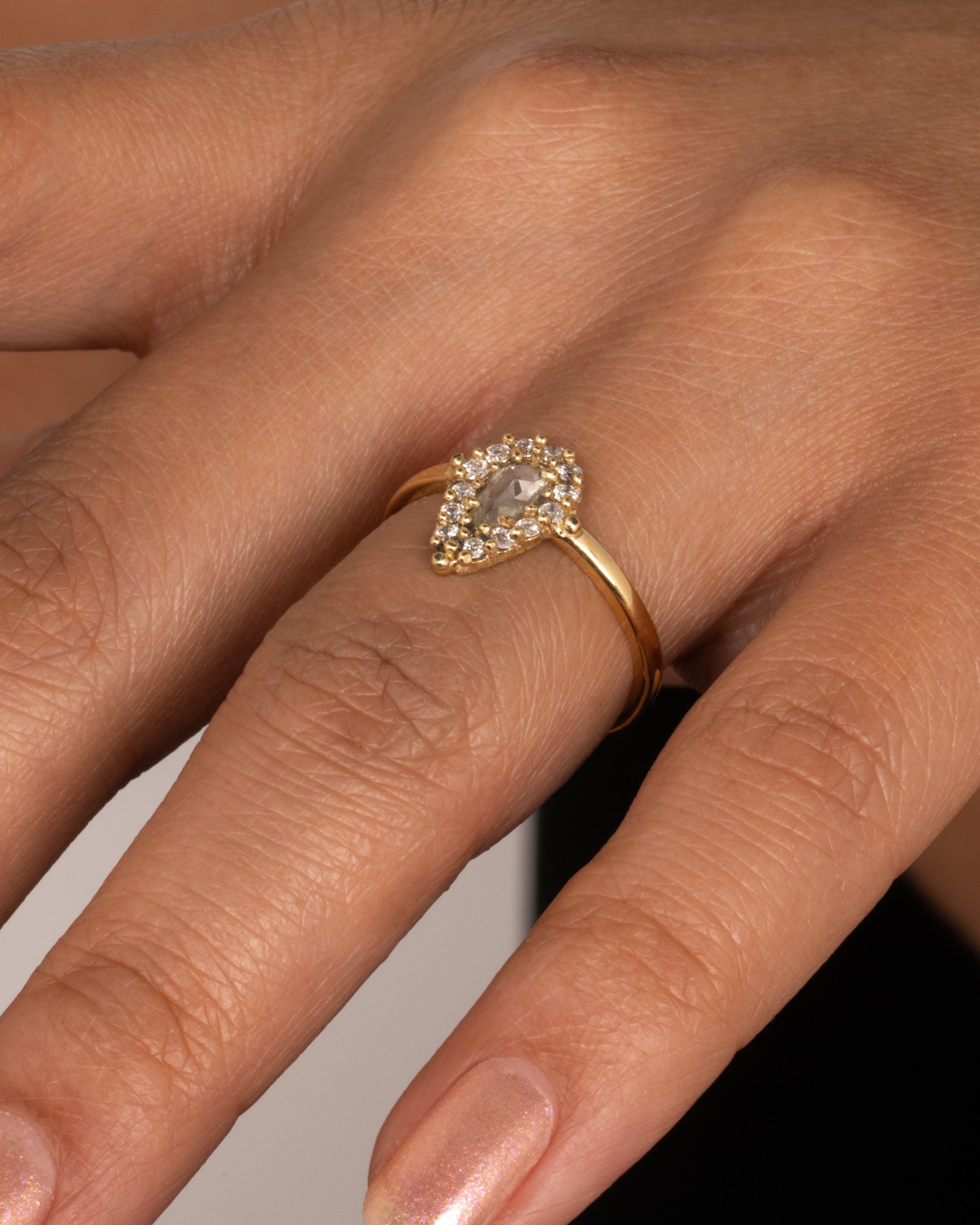 A yellow gold ring with a light champagne rose cut pear shaped diamond haloed by round diamonds. Shown from the front worn on hand.