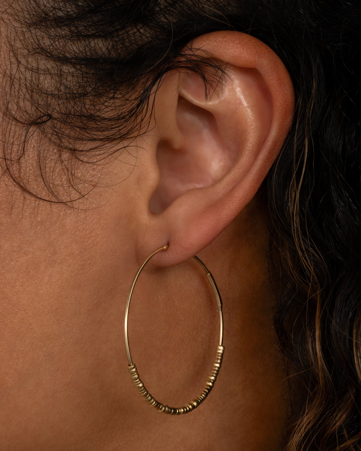 A yellow gold hoop earring with freely moving beads. Shown on a person from the side.