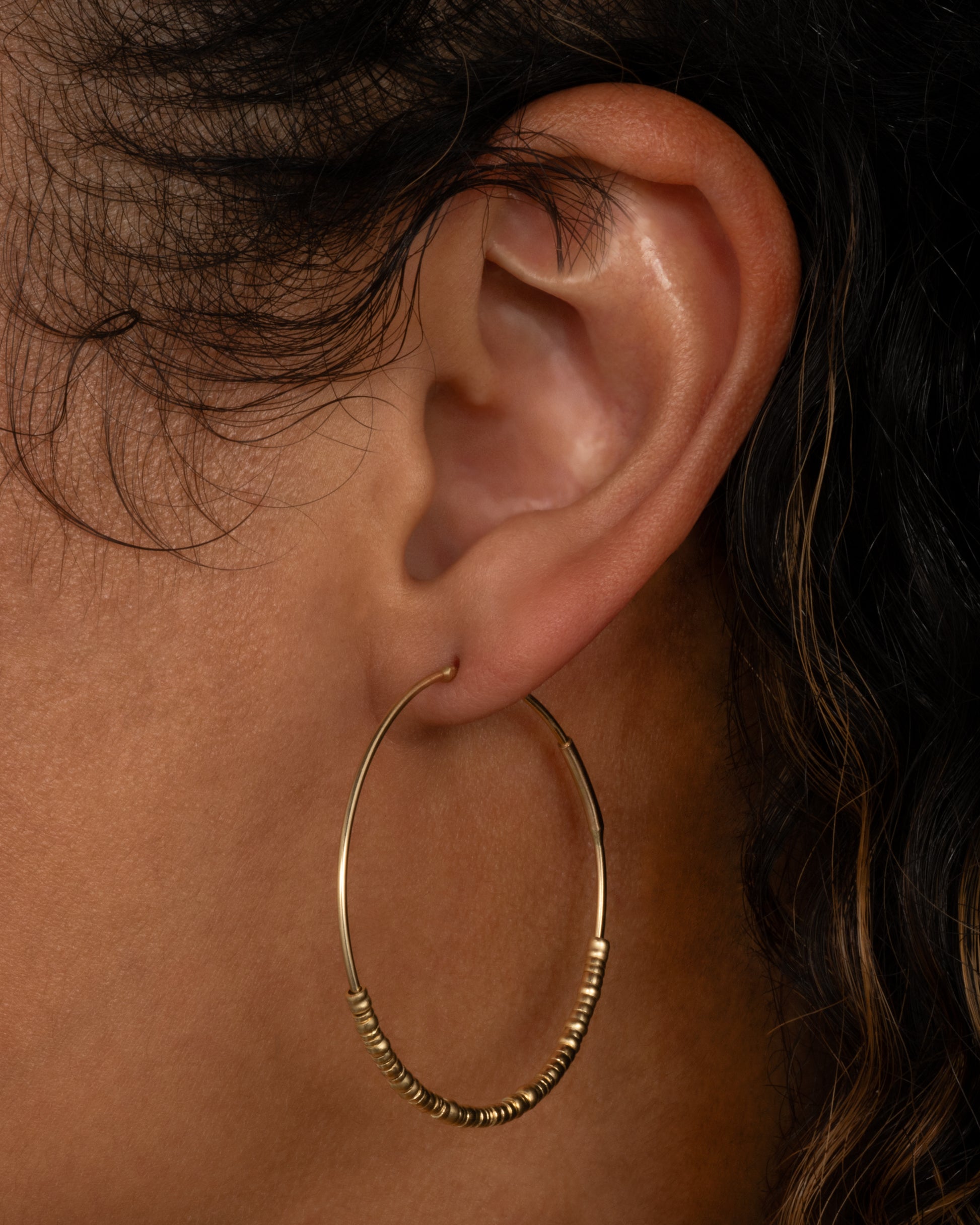 A yellow gold hoop earring with freely moving beads. Shown on a person from the side.