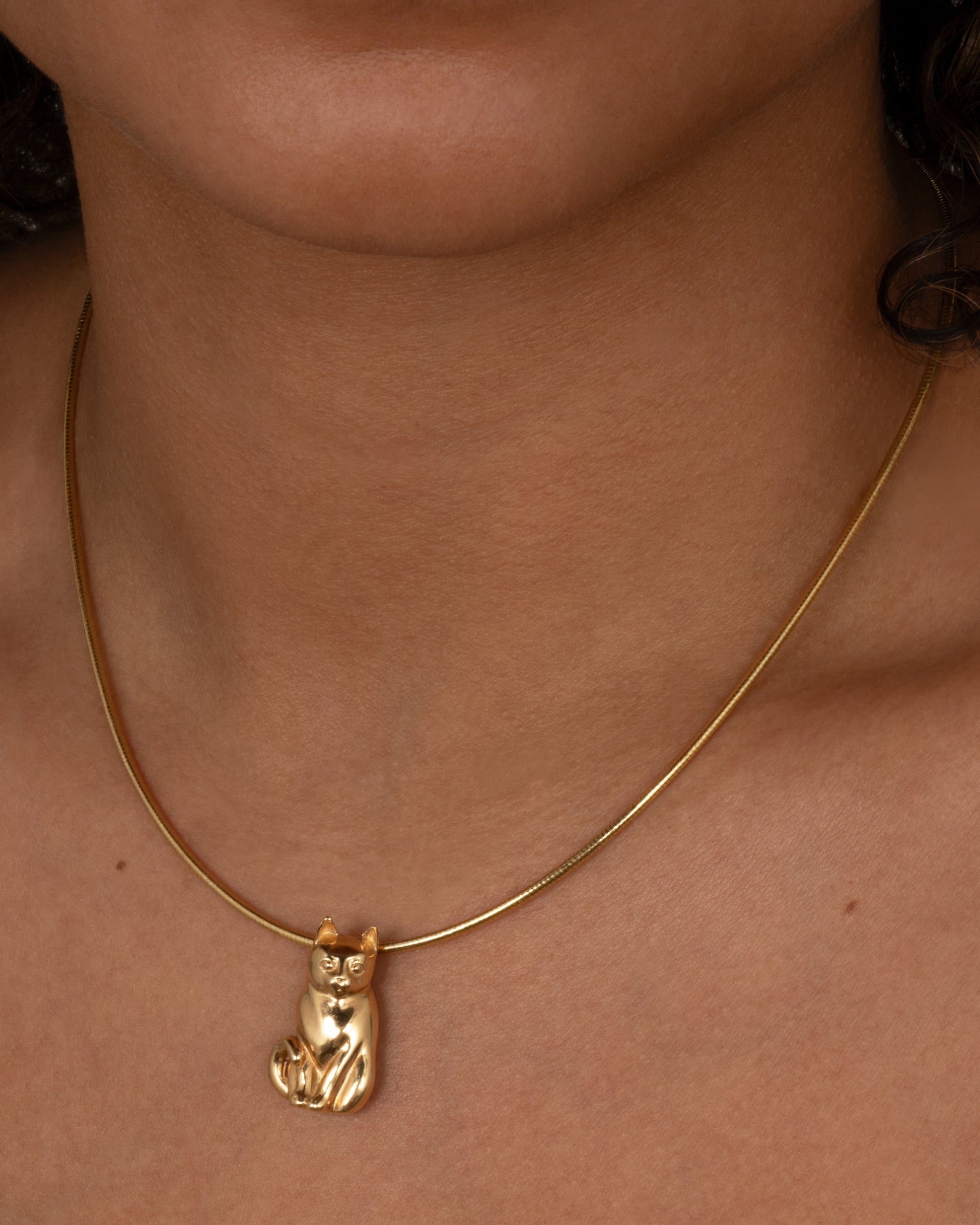 A yellow gold cat charm, shown worn on a chain around the neck.