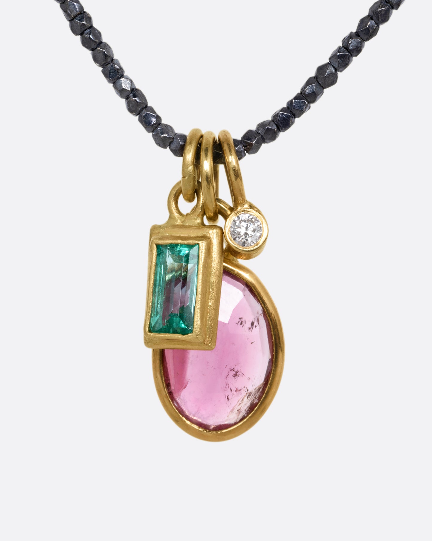 A necklace with three charms; pink tourmaline, emerald, and diamond with oxidized silver beads. Shown from the front.