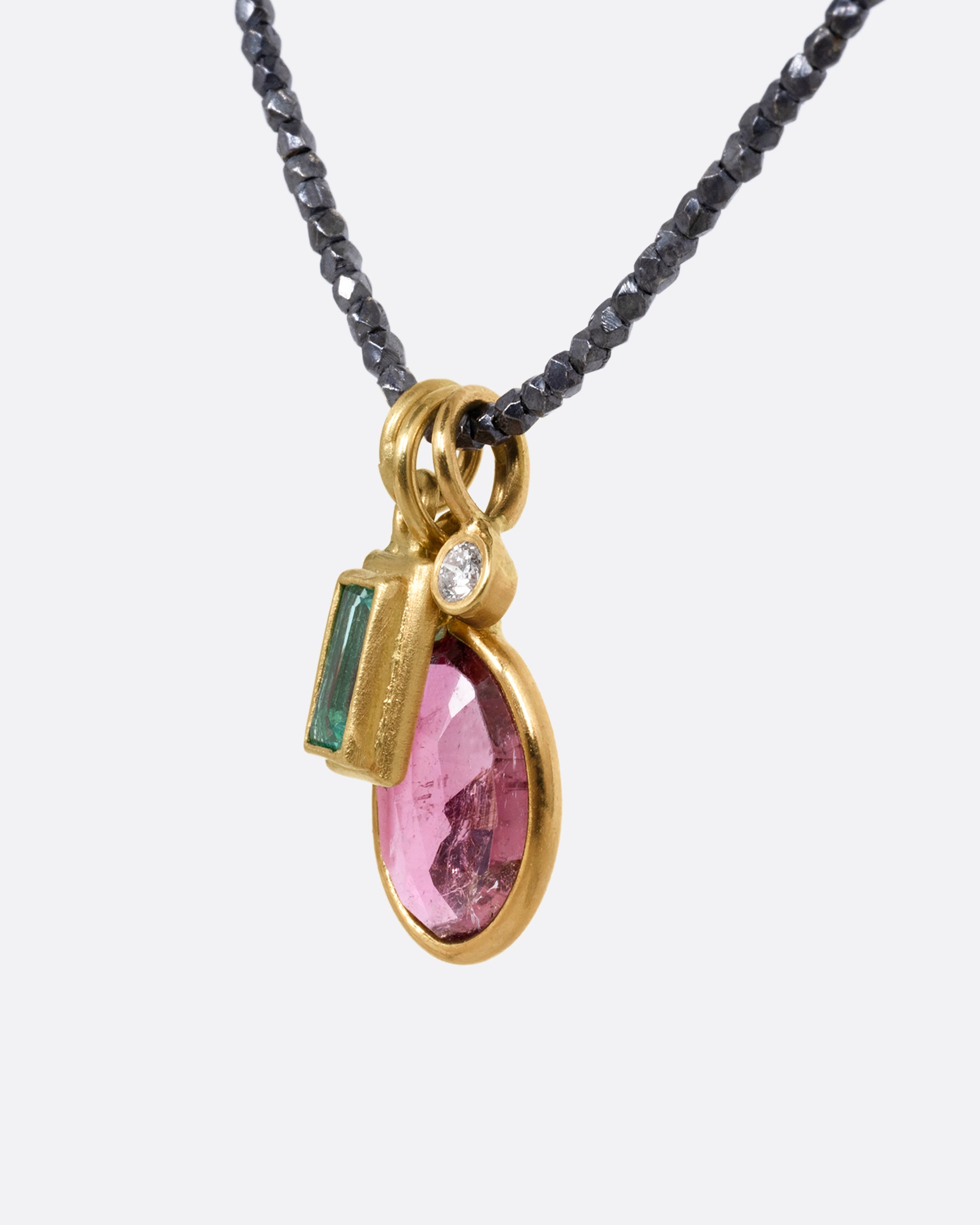 A necklace with three charms; pink tourmaline, emerald, and diamond with oxidized silver beads. Shown from the side.
