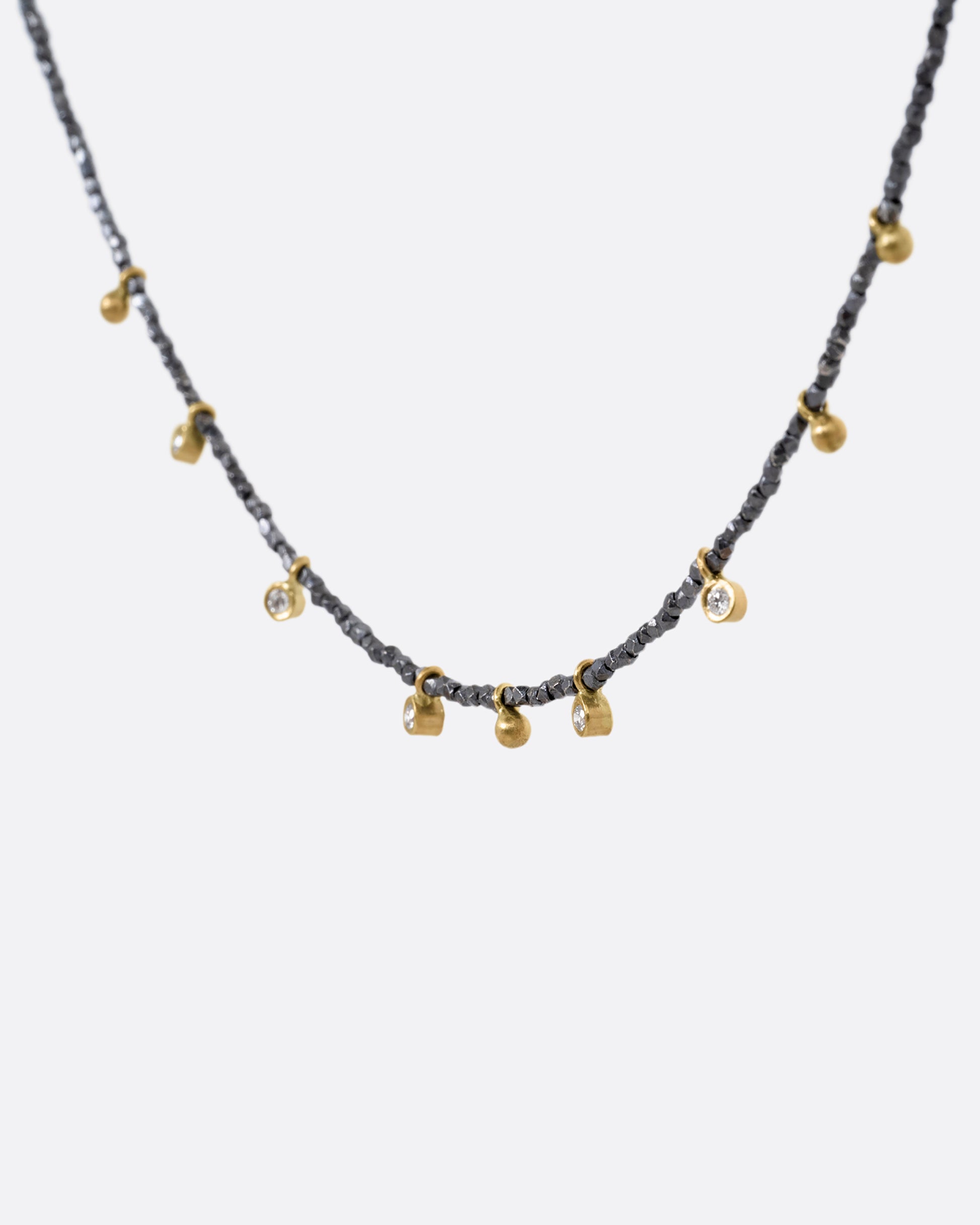 A necklace with five bezel set diamond charms and four gold drops interspersed among oxidized silver beads. Shown from the side.