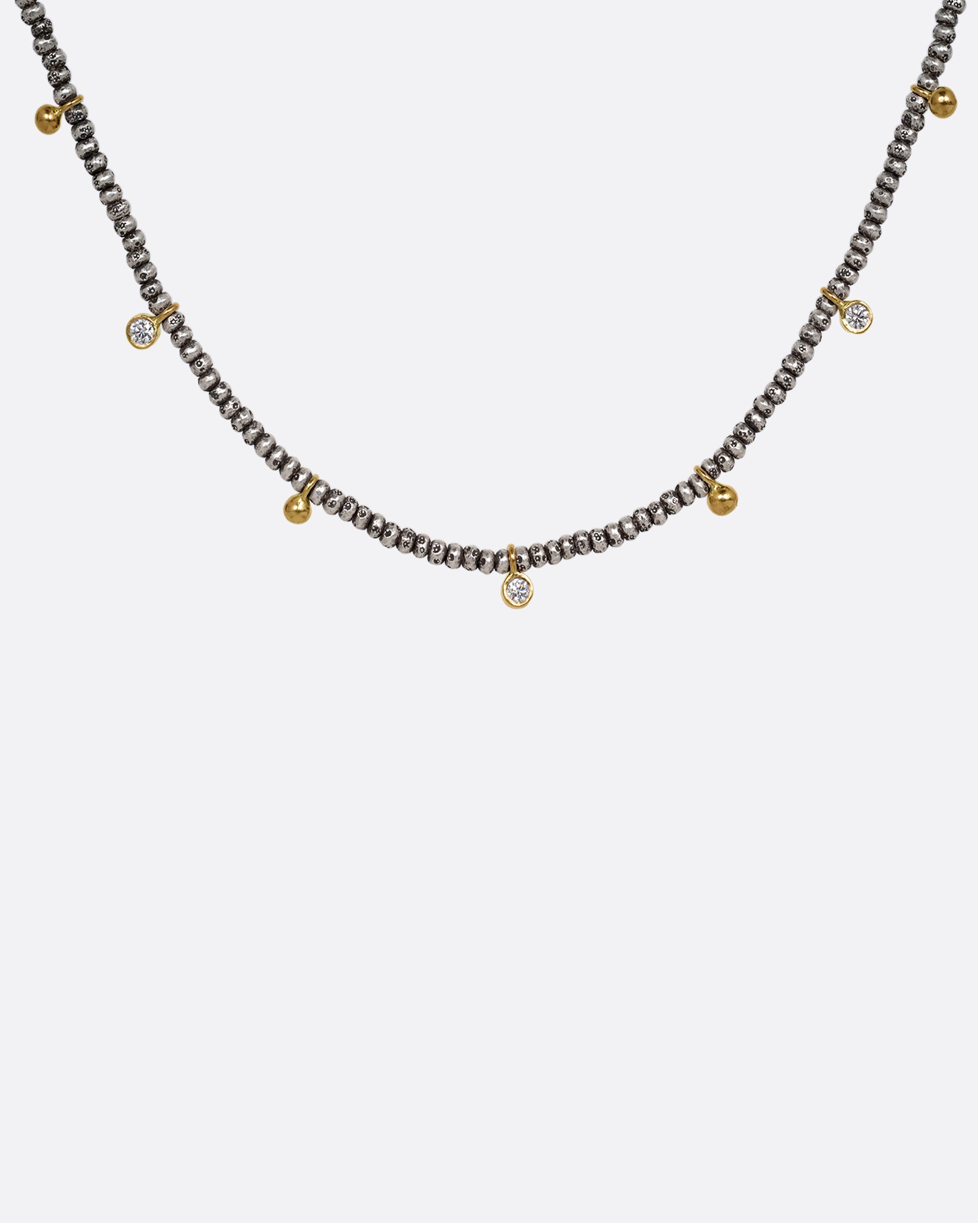 A necklace with nine brilliant cut diamond charms and ten gold drops among oxidized silver beads. Shown from the front.