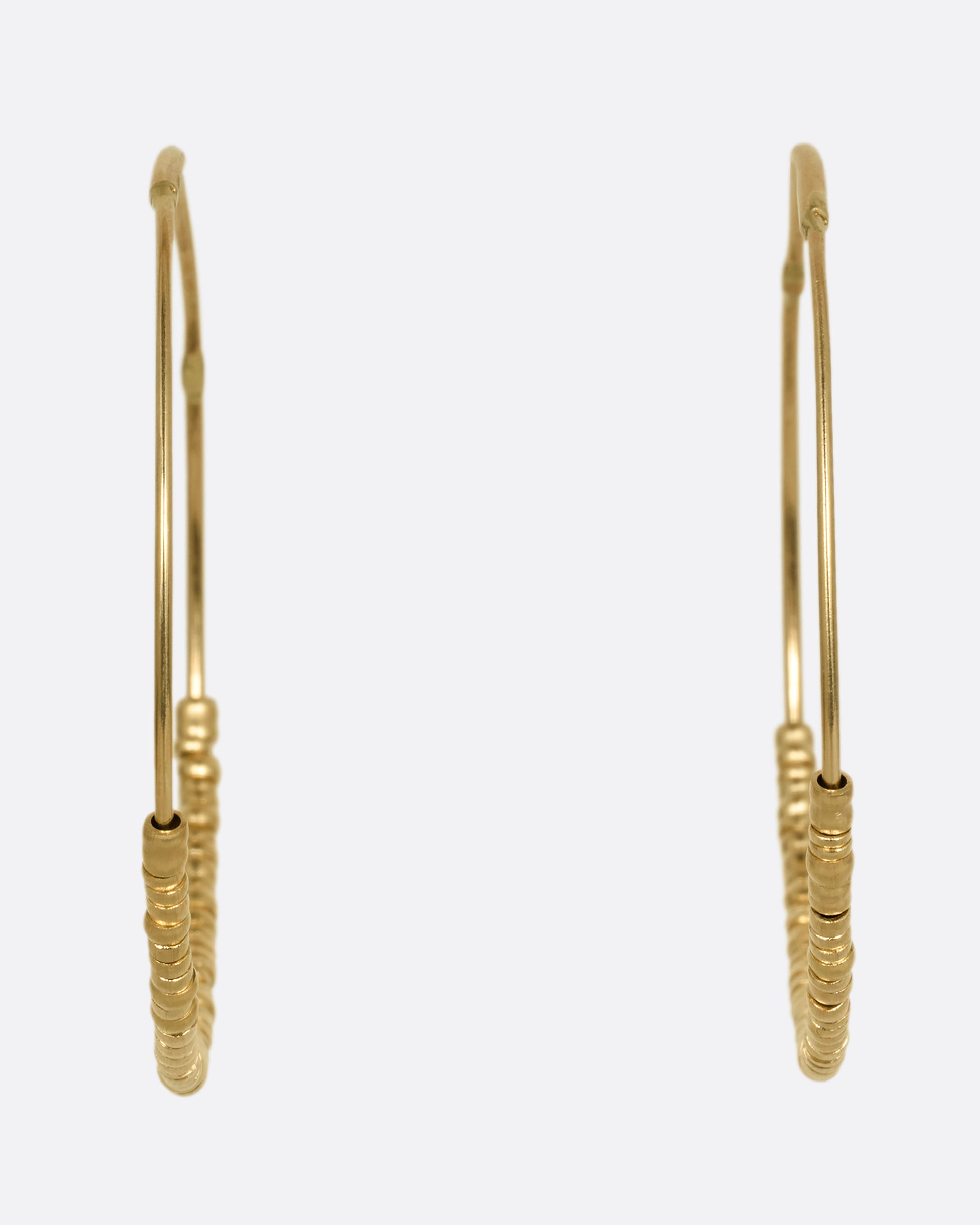 A pair of yellow gold hoop earrings with freely moving beads. Shown from the front.