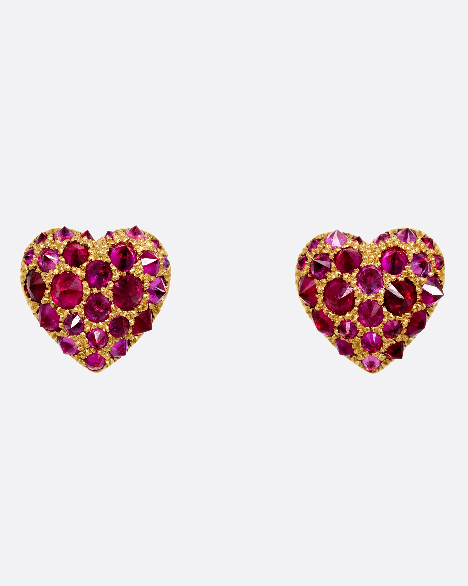A pair of yellow gold heart shaped stud earrings with reverse set rubies of varying sizes set into them. Shown from the front.