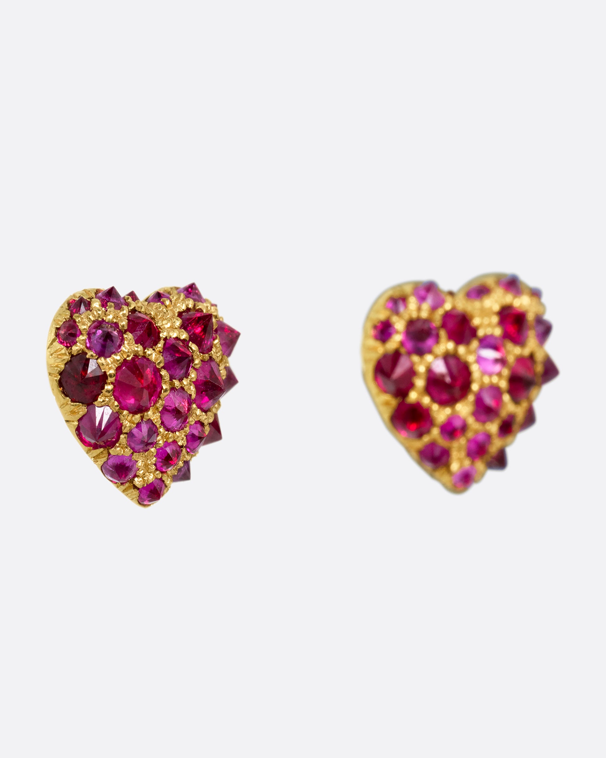 A pair of yellow gold heart shaped stud earrings with reverse set rubies of varying sizes set into them. Shown from the side.