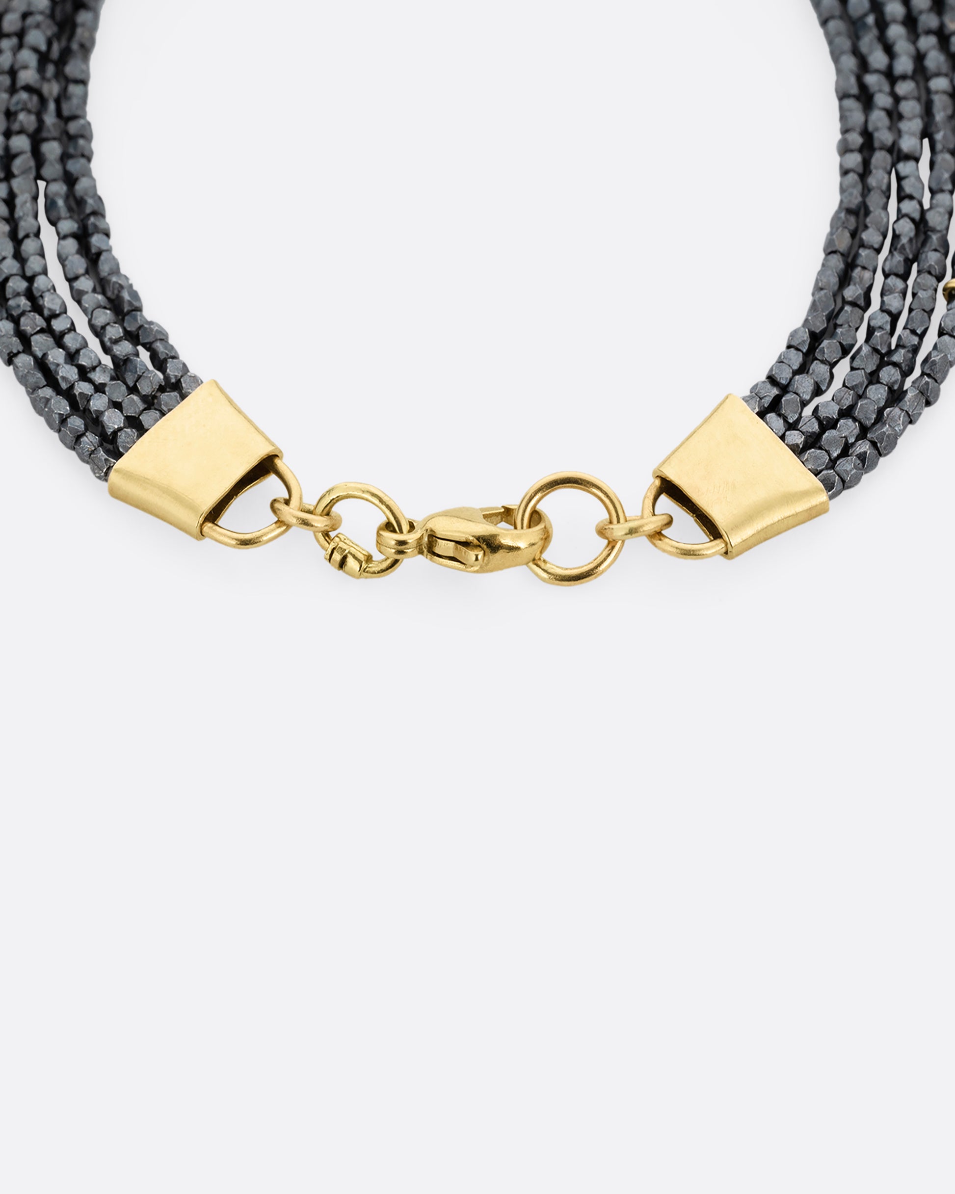 A close up of a bracelet with five strands of oxidized silver beads converging at  yellow gold capped ends with a lobster clasp. Shown from the top.
