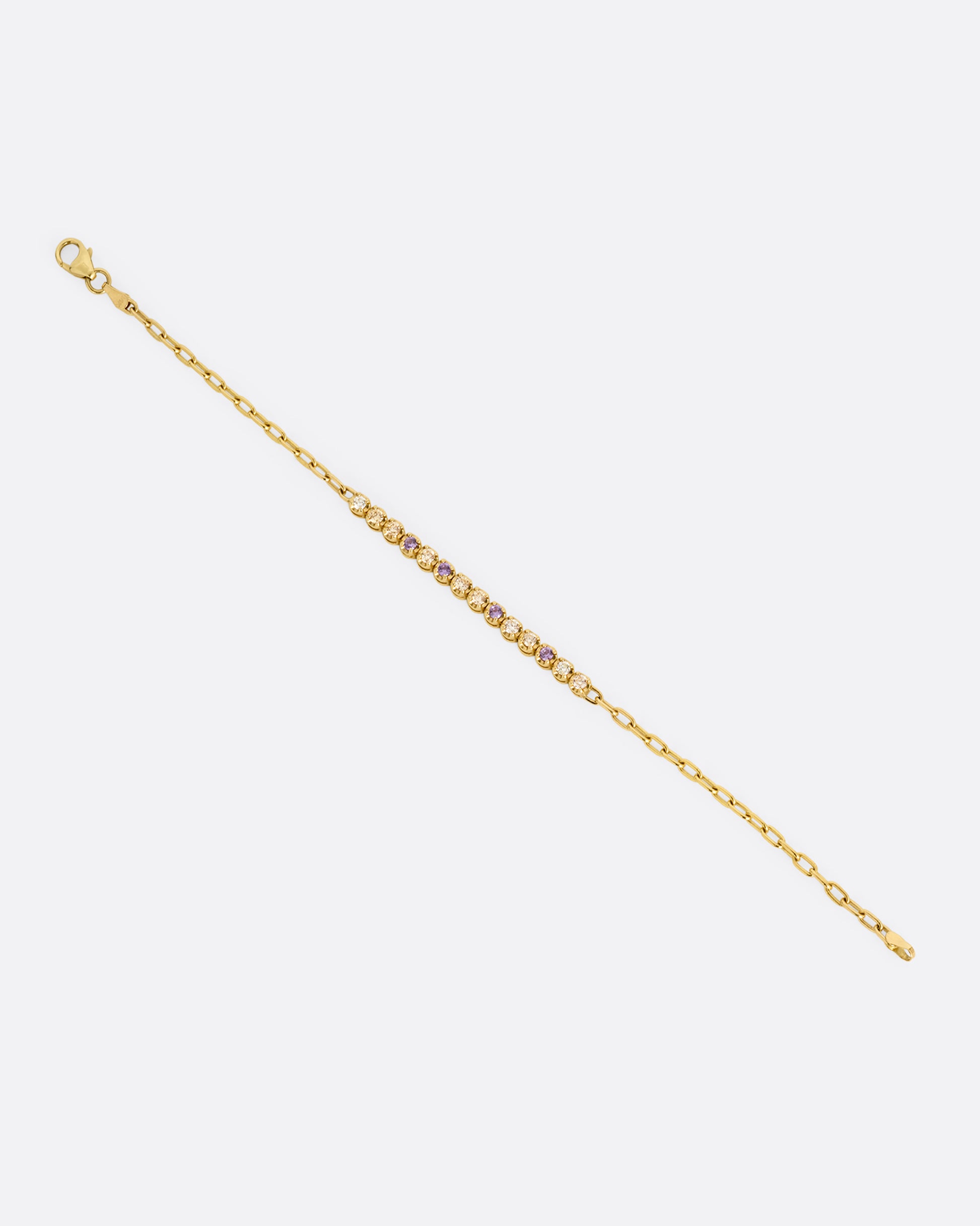 A yellow gold partial tennis bracelet with peach and yellow diamonds and purple sapphires. Shown from the front.