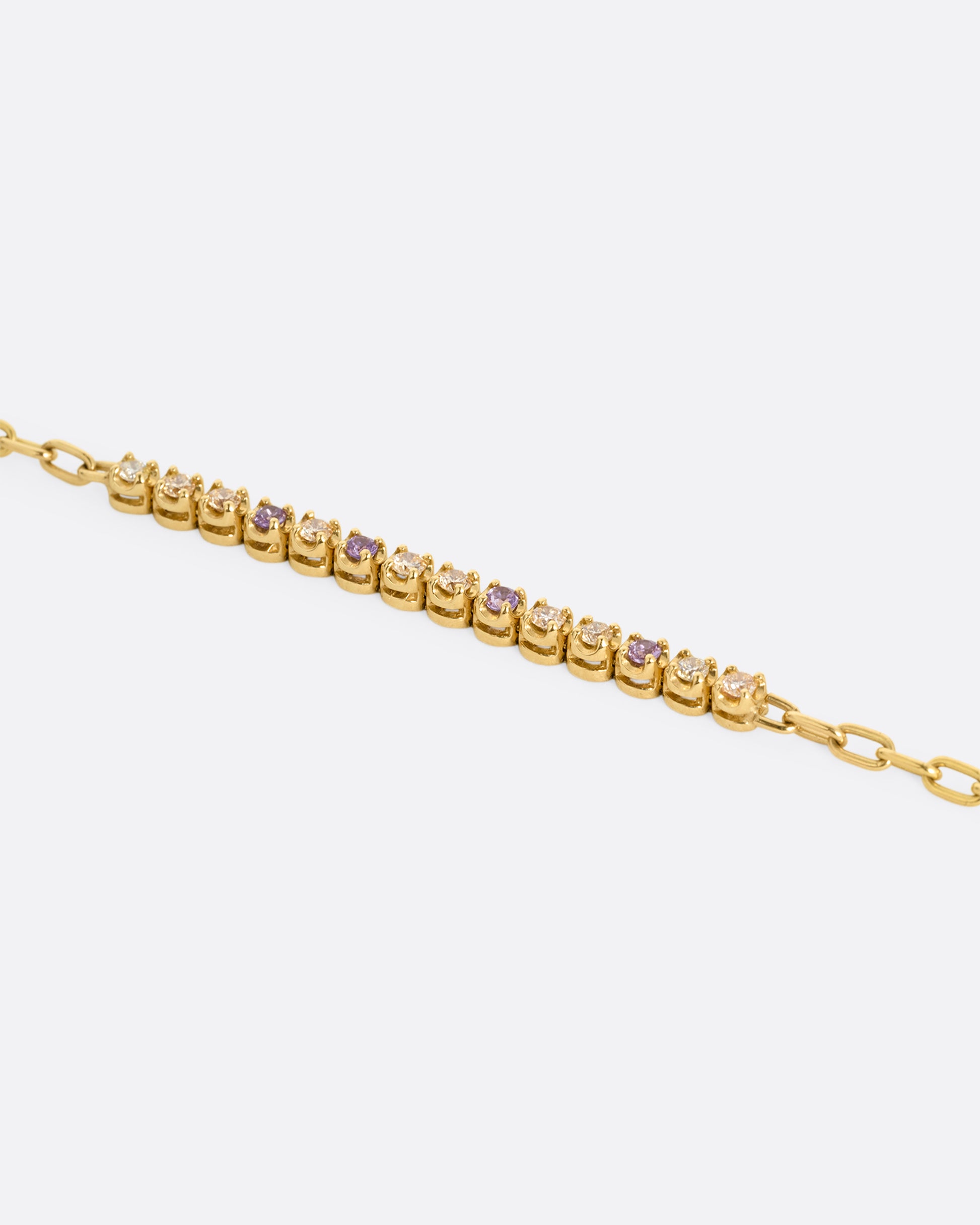 A close up of a yellow gold partial tennis bracelet with peach and yellow diamonds and purple sapphires. 