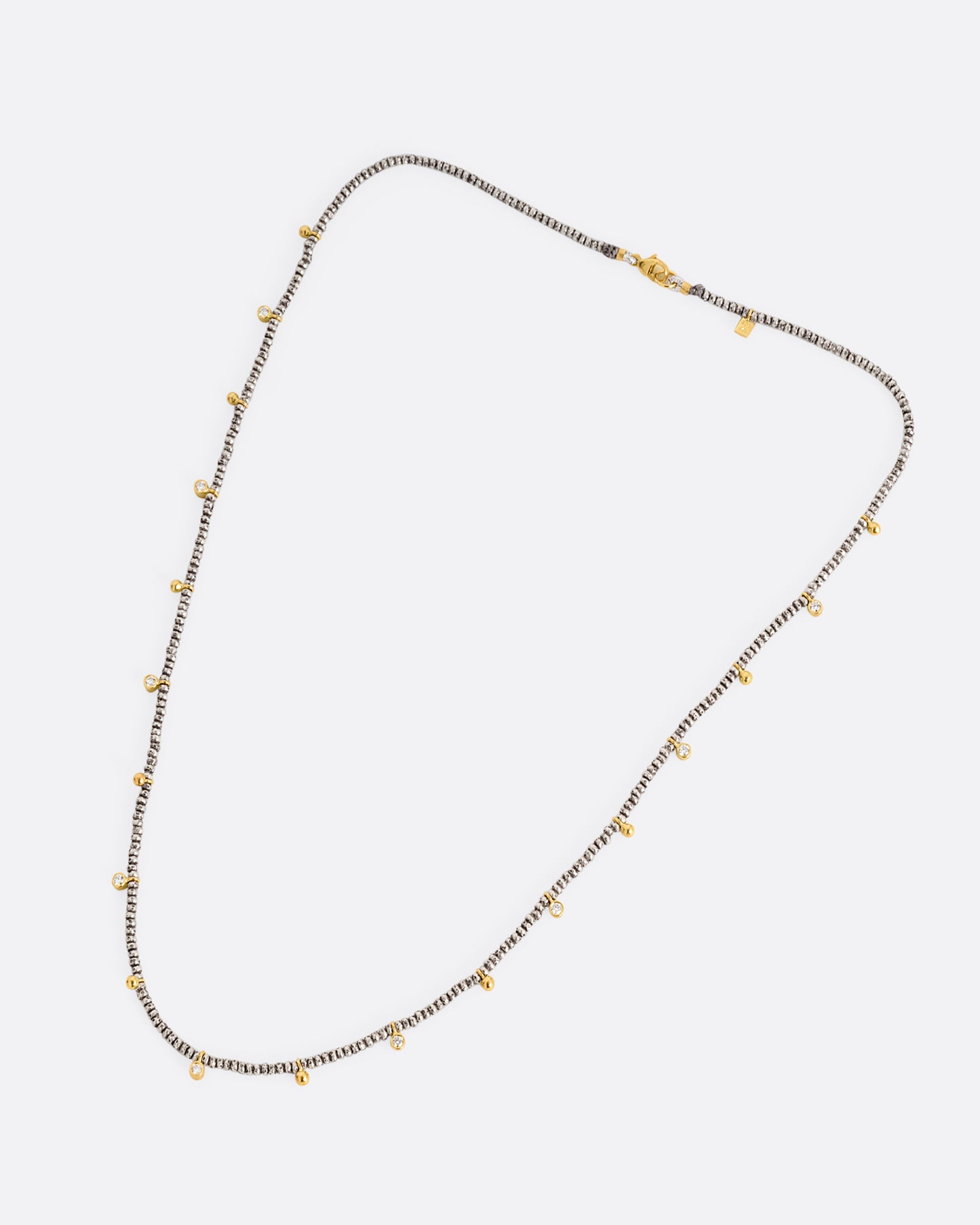 A necklace with nine brilliant cut diamond charms and ten gold drops among oxidized silver beads. Shown lying flat from the front.