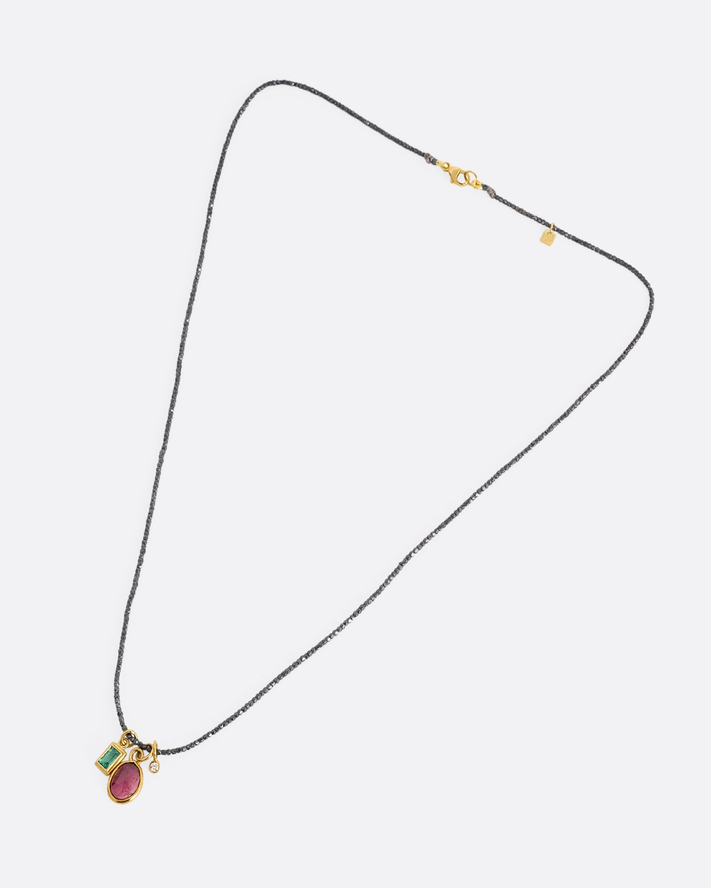 A necklace with three charms; pink tourmaline, emerald, and diamond with oxidized silver beads. Shown lying flat.