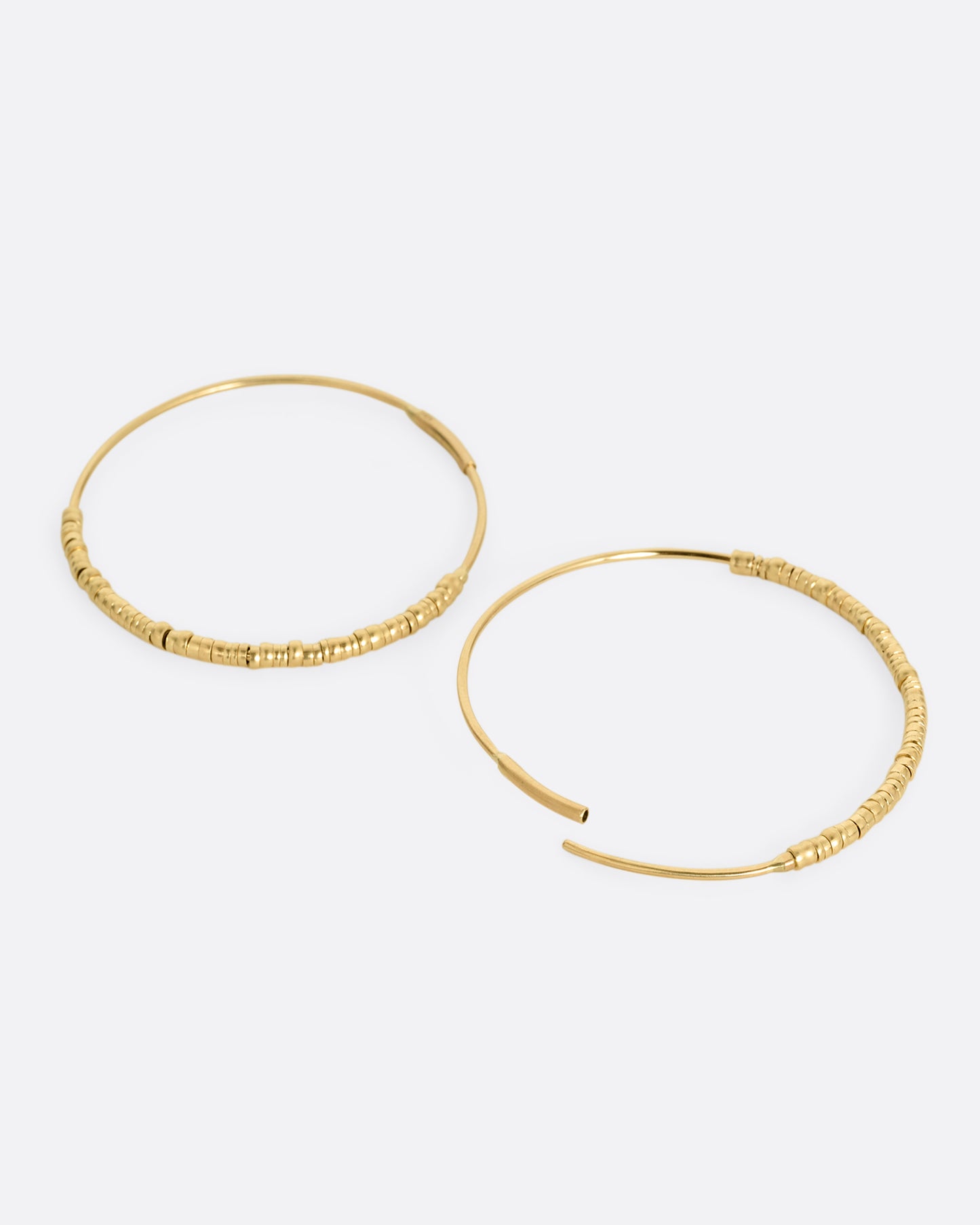 A pair of yellow gold hoop earrings with freely moving beads. Shown lying flat from the side with one hoop open.