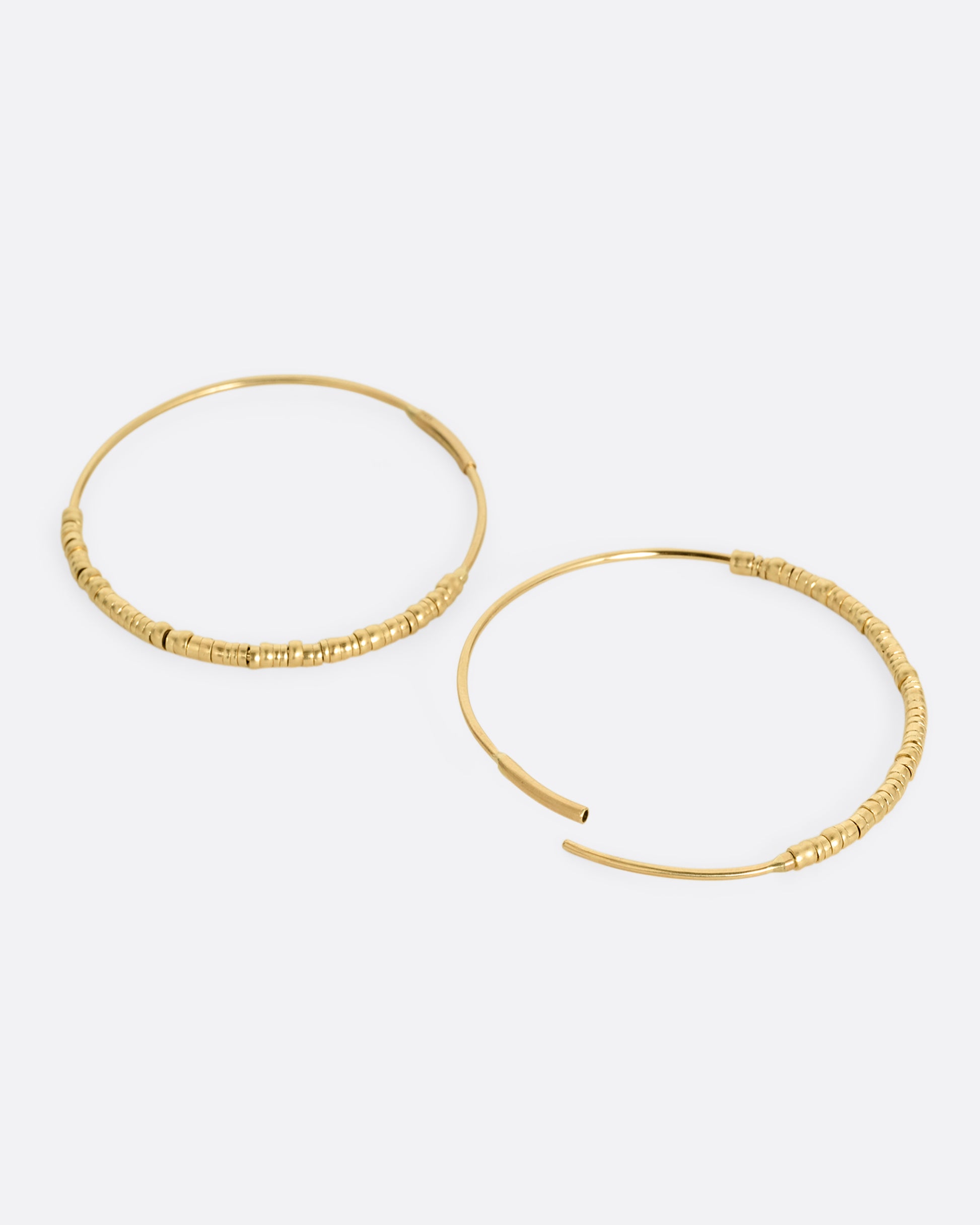 A pair of yellow gold hoop earrings with freely moving beads. Shown lying flat from the side with one hoop open.
