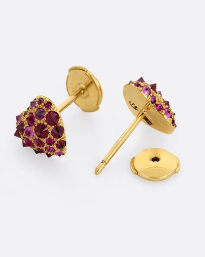 A pair of yellow gold heart shaped stud earrings with reverse set rubies of varying sizes set into them. One earring is shown from the front, the other is shown open from the back.
