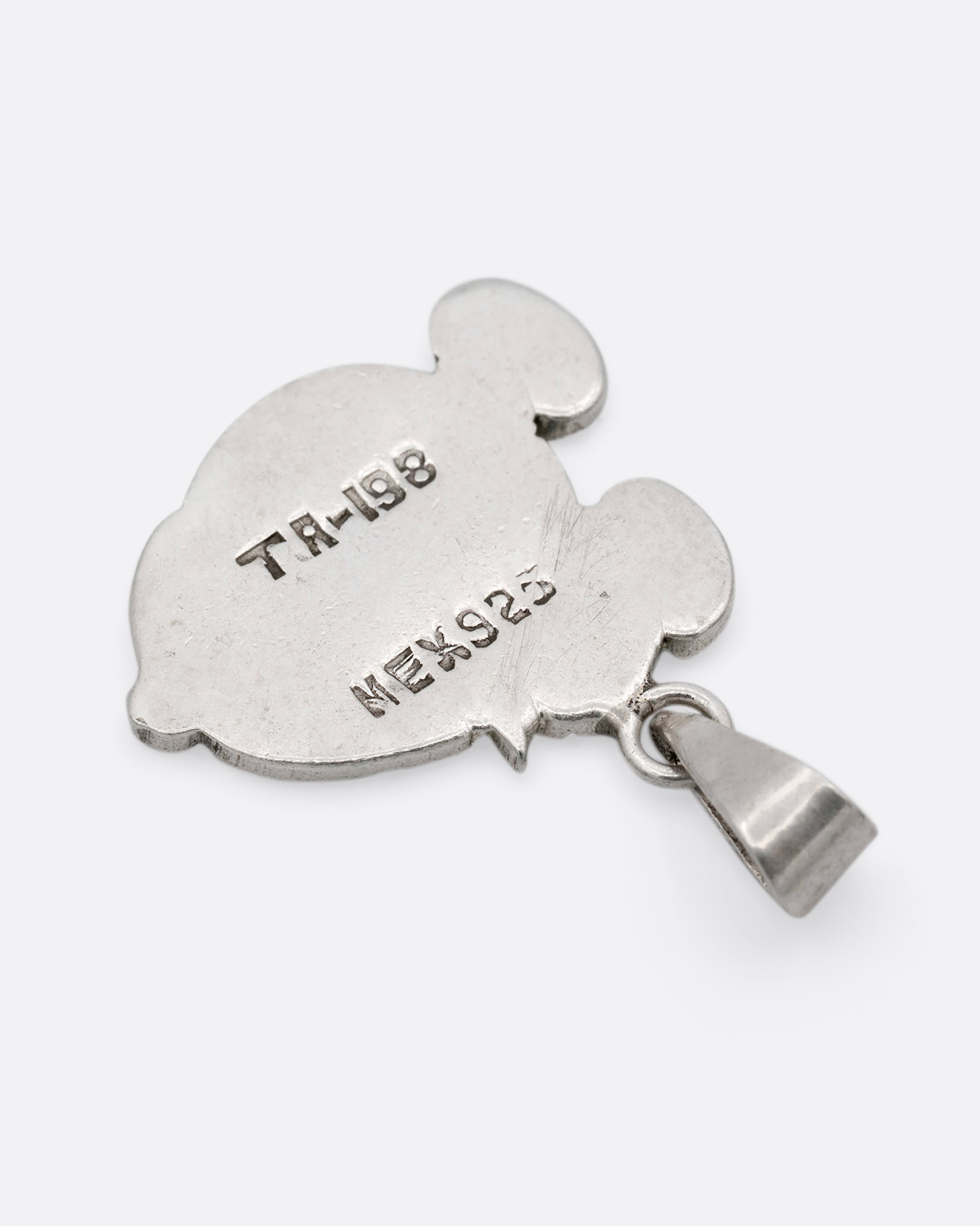 A silver hand carved Mickey Mouse profile charm with a crown. Shown from the back.
