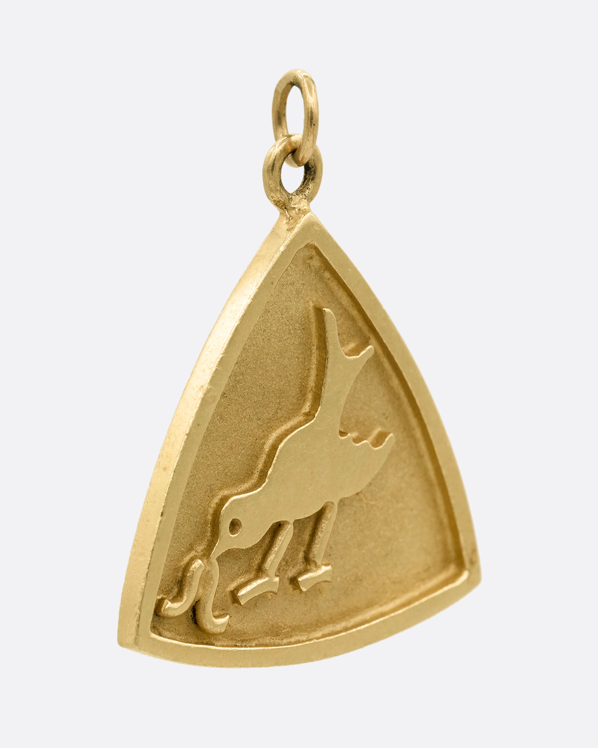 A yellow gold triangular charm with a bird getting worm on the front. Shown from the side.