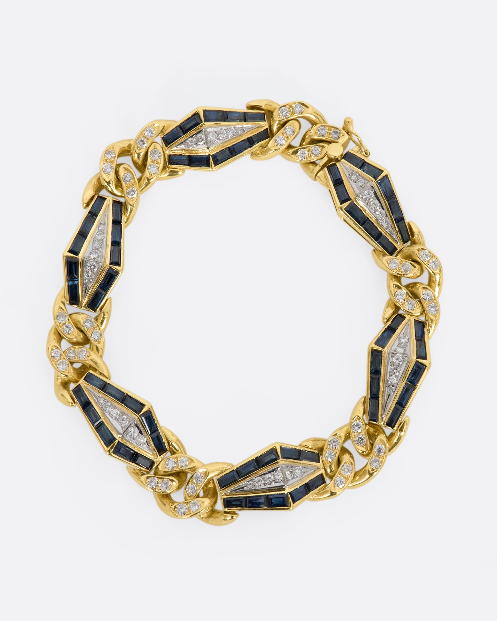 Yellow gold curb chain bracelet with sapphire baguette stations and diamonds throughout. View from above, closed, laying flat.