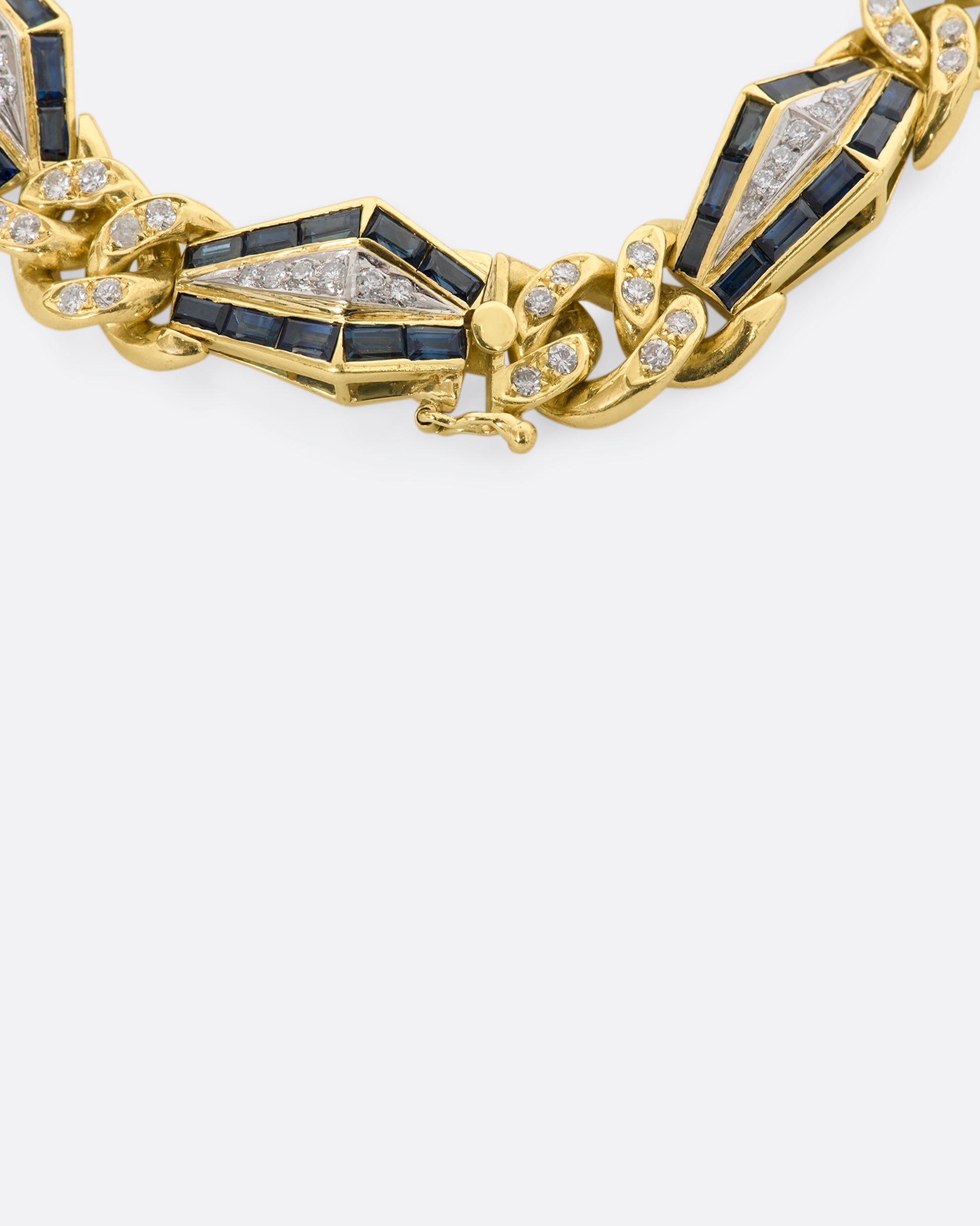 Yellow gold curb chain bracelet with sapphire baguette stations and diamonds throughout. View of the closure.