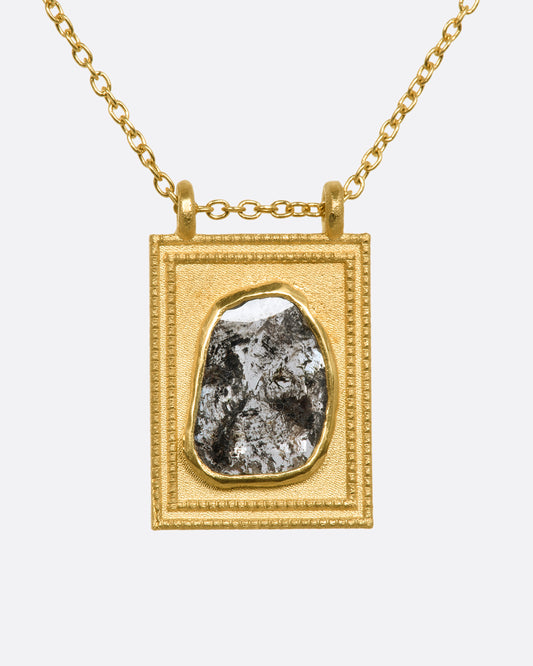 A yellow gold rectangular pendant with a textured border featuring a rose cut salt and pepper diamond hanging from a cable chain. View from the front.