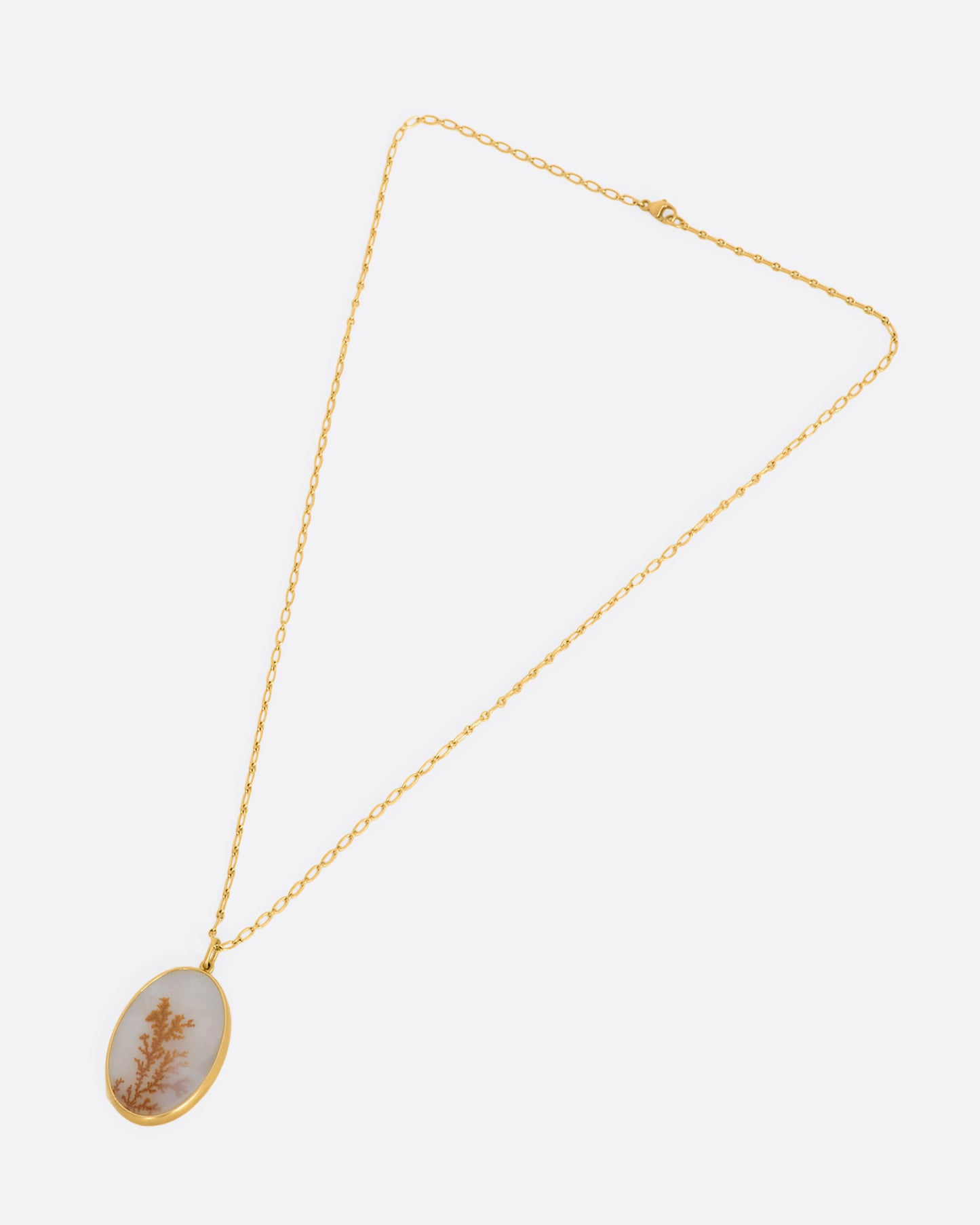 A yellow gold necklace with oval dendritic agate pendant on a yellow gold chain. View from above of the entire necklace, closed.