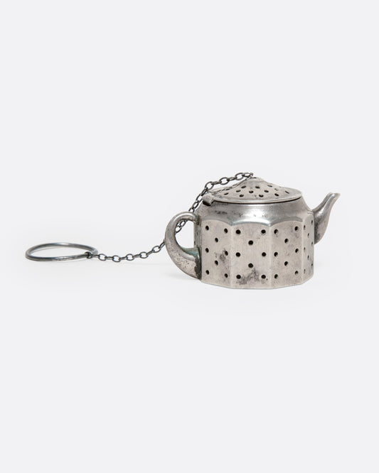A silver teapot shaped infuser, topped with a hinged lid, shown from the side.
