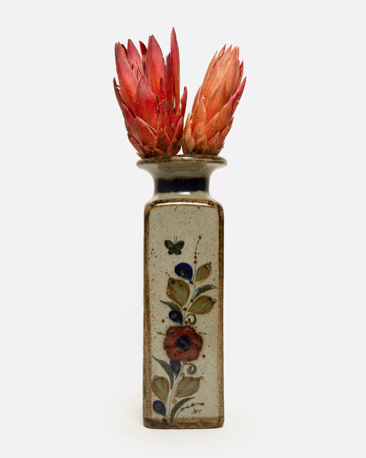A ceramic vase with floral design containing two red protea flowers, shown from the front.
