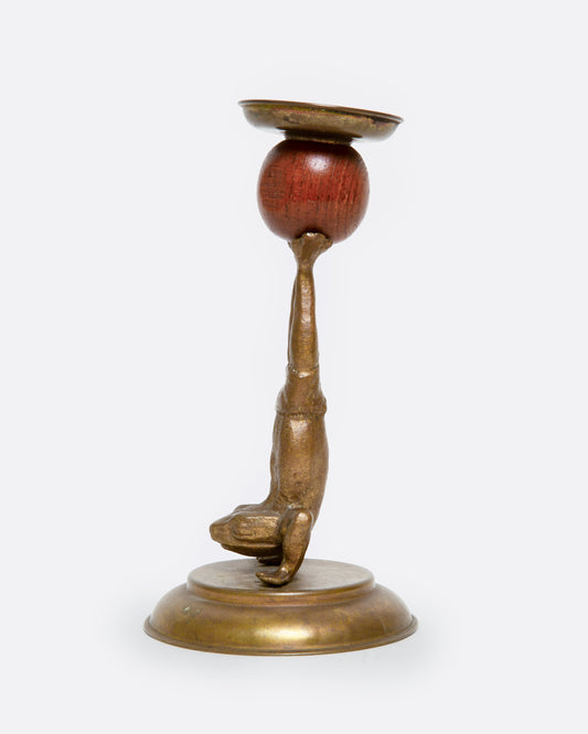 A brass and wooden frog candlestick holder shown from the side.