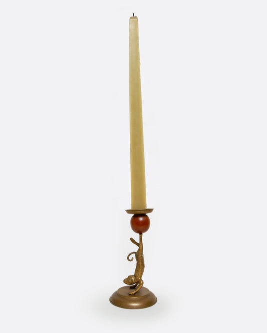 A brass and wooden monkey candlestick holder shown from the side with a taper in it.