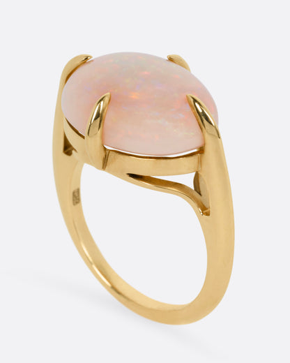 A yellow gold ring with a prong set opal, shown from the side standing up.