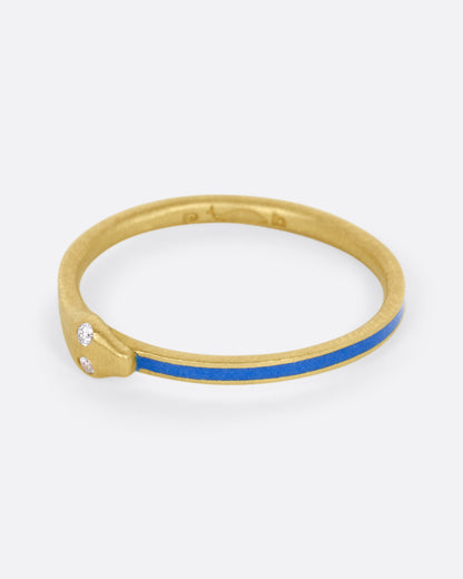 A yellow gold ouroboros ring with diamond eyes and blue enamel, shown from the side.