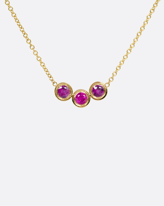 A yellow gold cable chain necklace with a trio of bezel set rubies at the center, shown from the front.