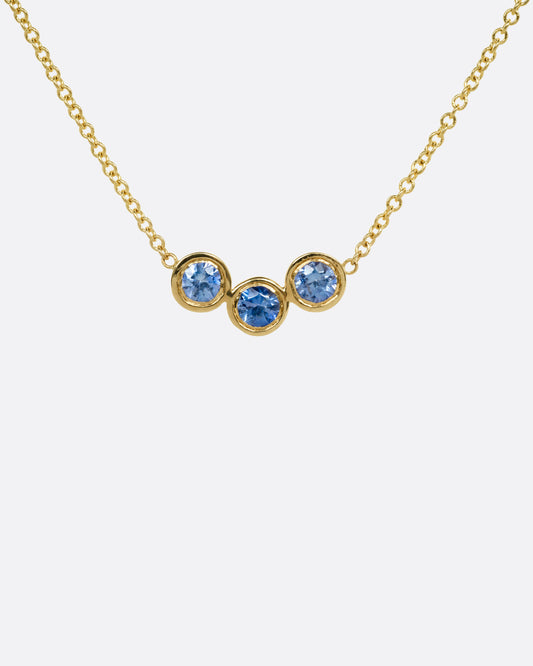 A yellow gold cable chain necklace with a trio of bezel set sapphires at the center, shown from the front.