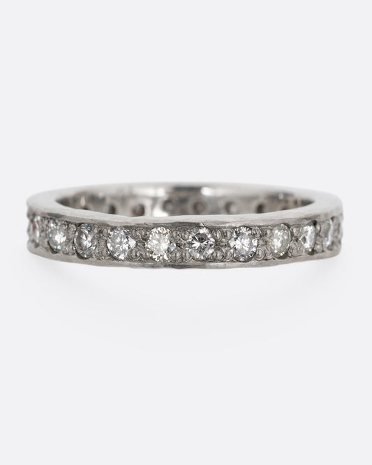 A platinum band with hammered edges and a darkened center with diamonds throughout. Shown from the front.