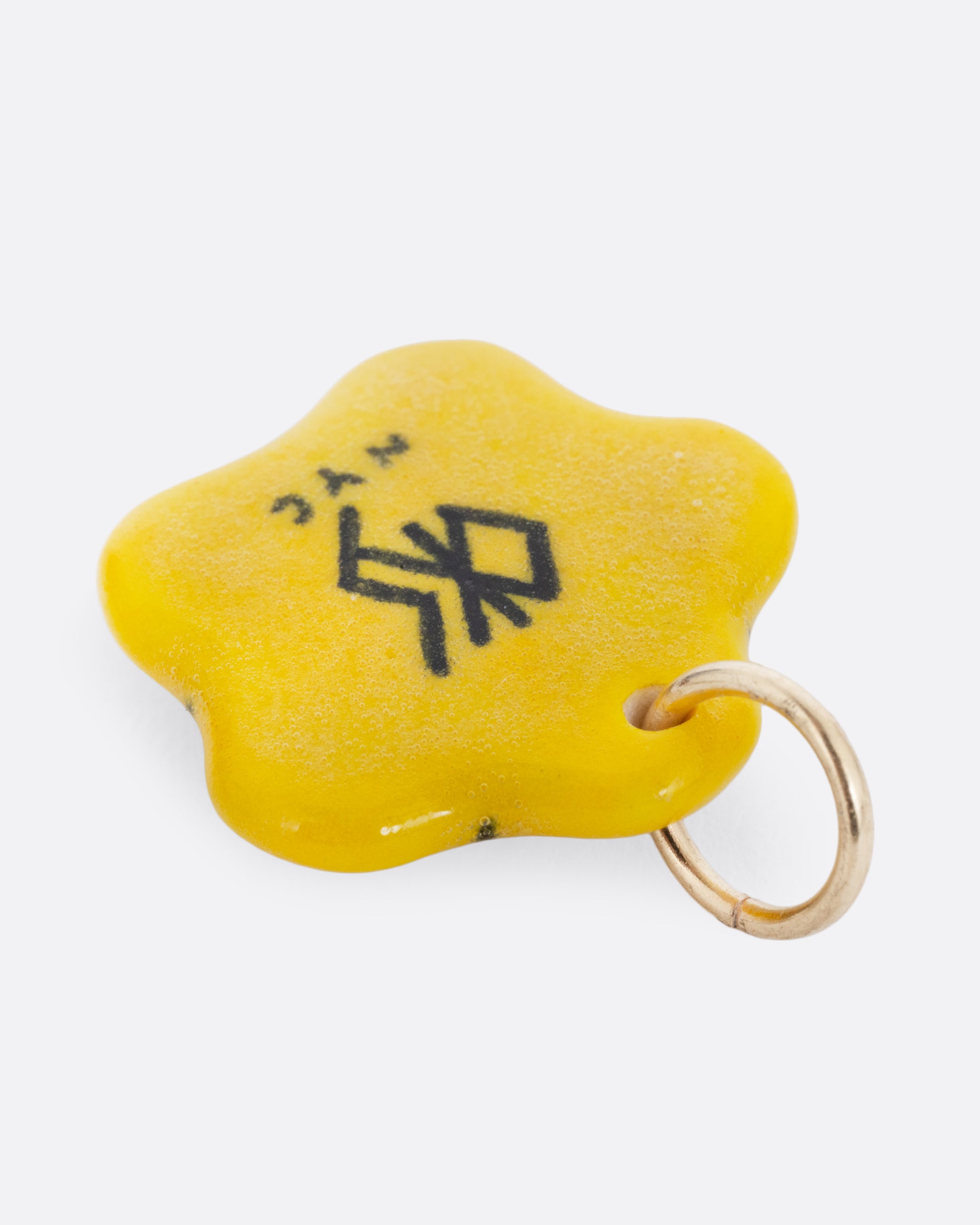 A yellow flower porcelain flower charm with a face at the center. Shown from the back.