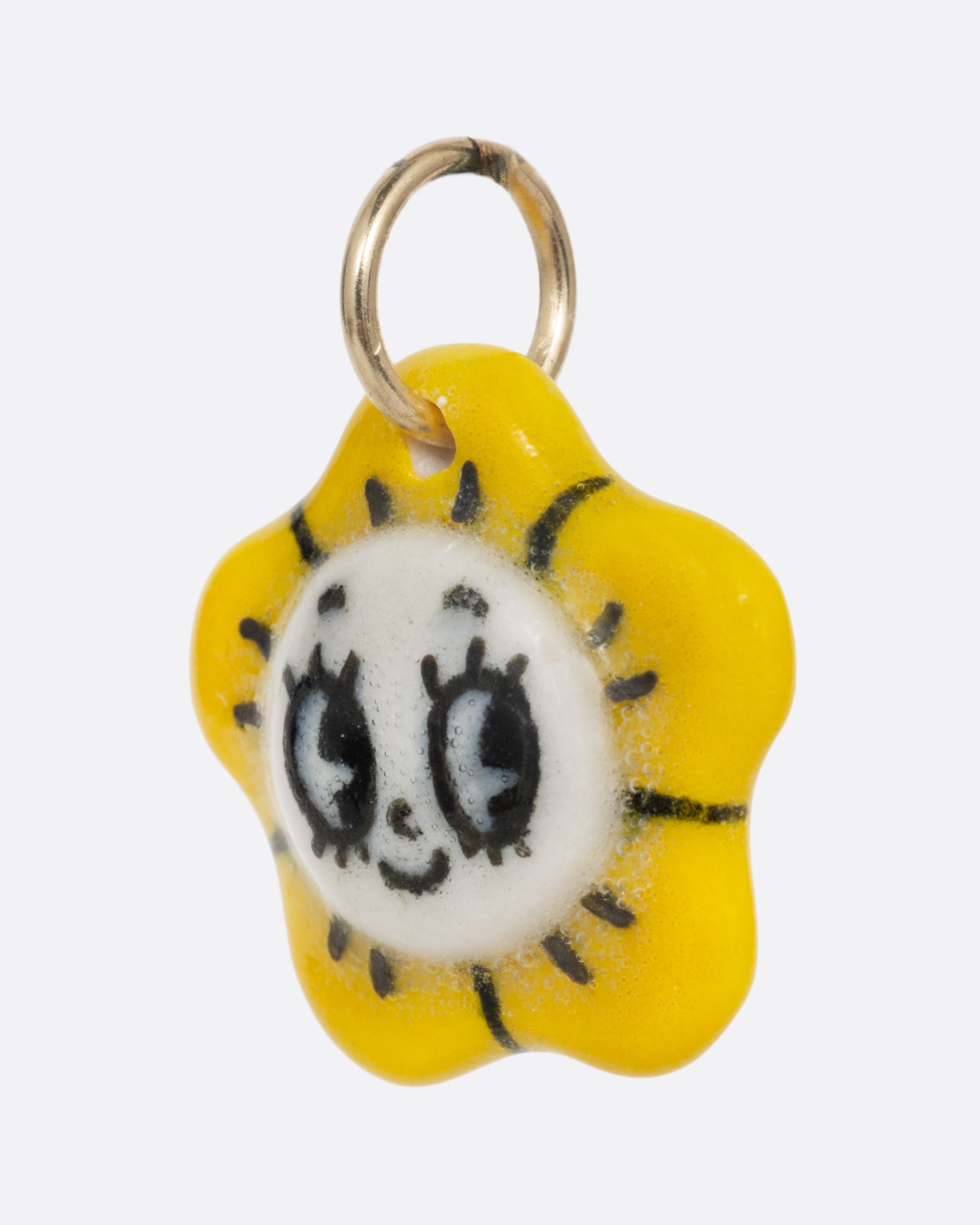 A yellow flower porcelain flower charm with a face at the center. Shown from the side.