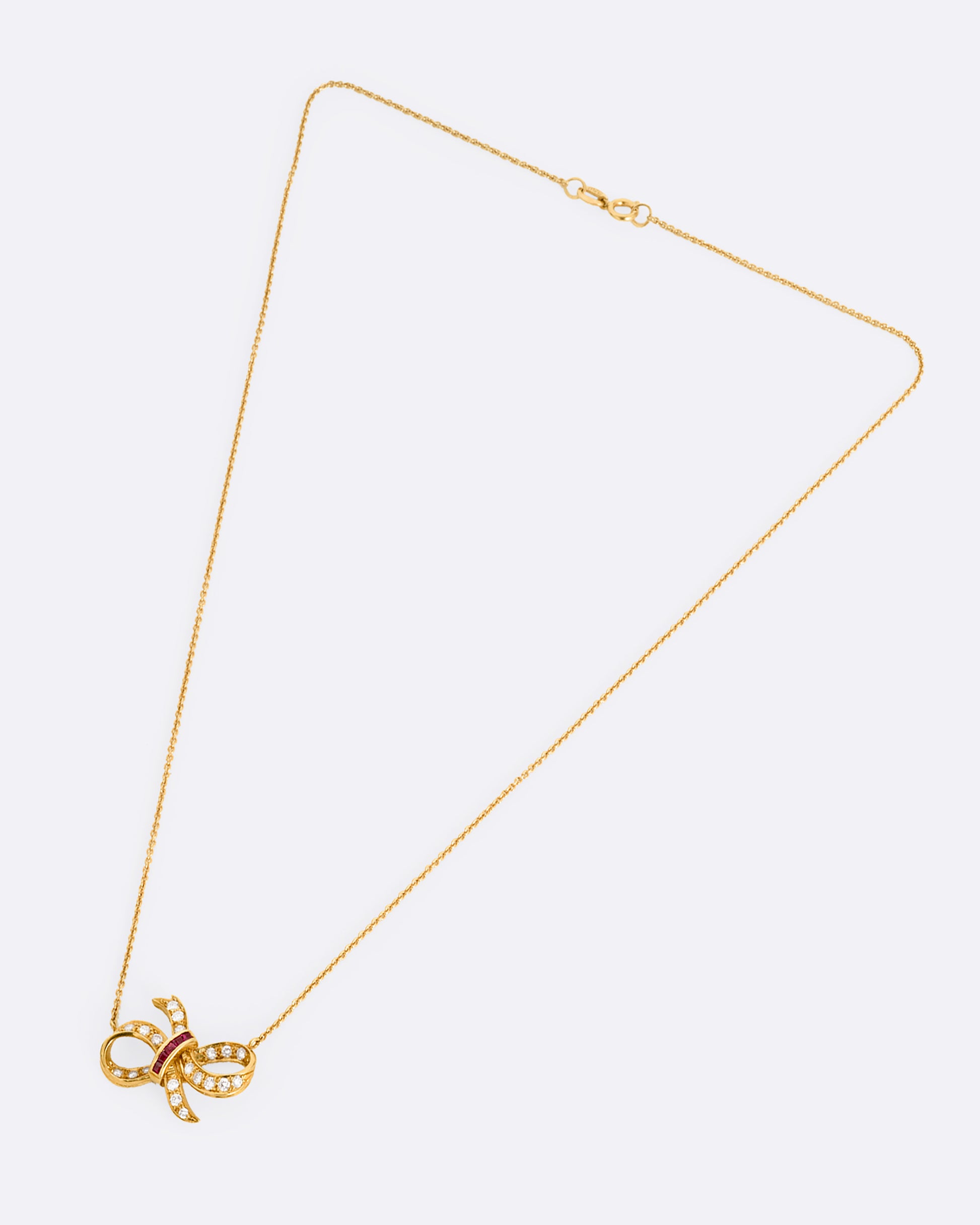 A yellow gold cable chain necklace with a diamond and ruby studded bow at the center. Shown from the front.
