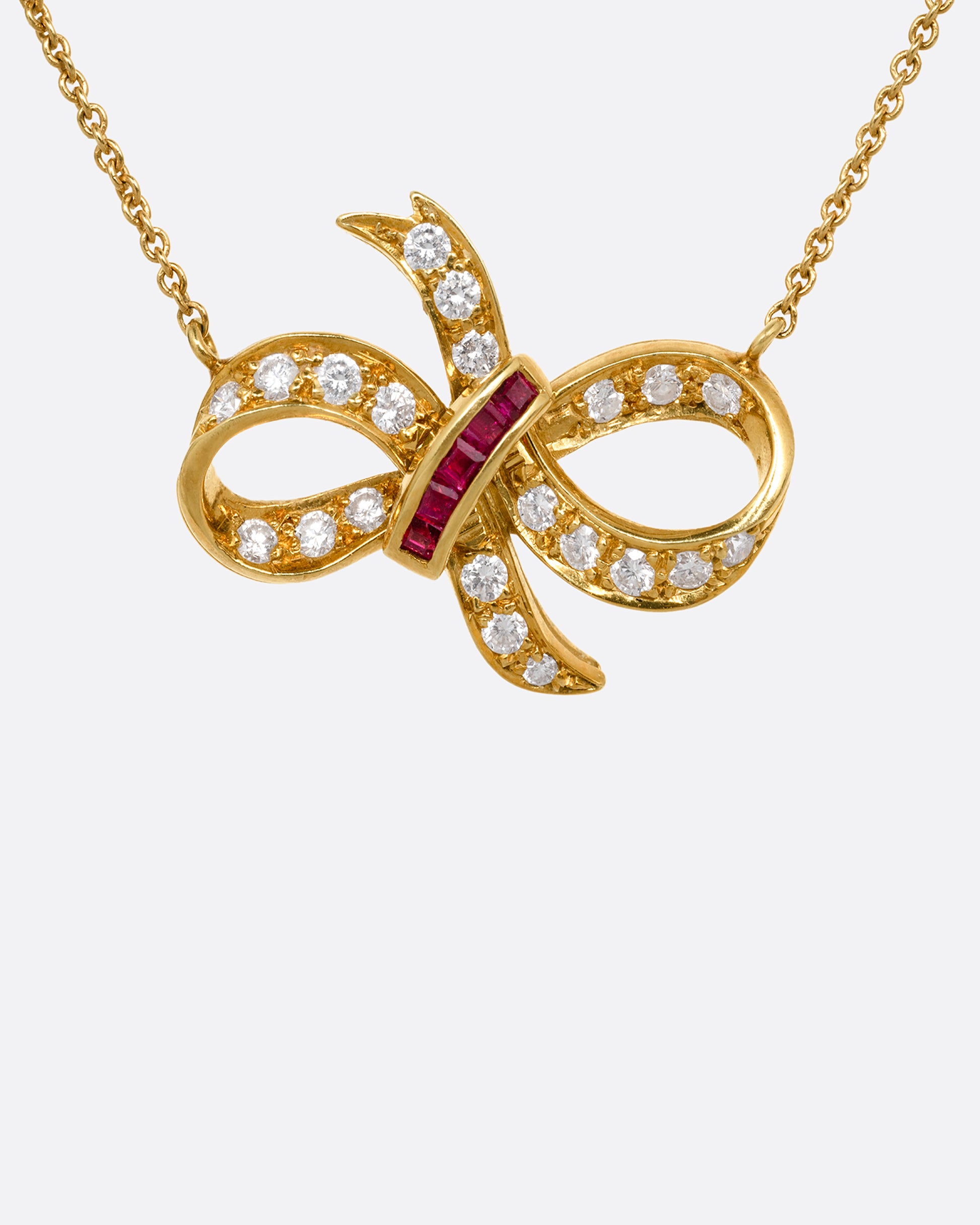 A yellow gold cable chain necklace with a diamond and ruby studded bow at the center. Shown from the front.