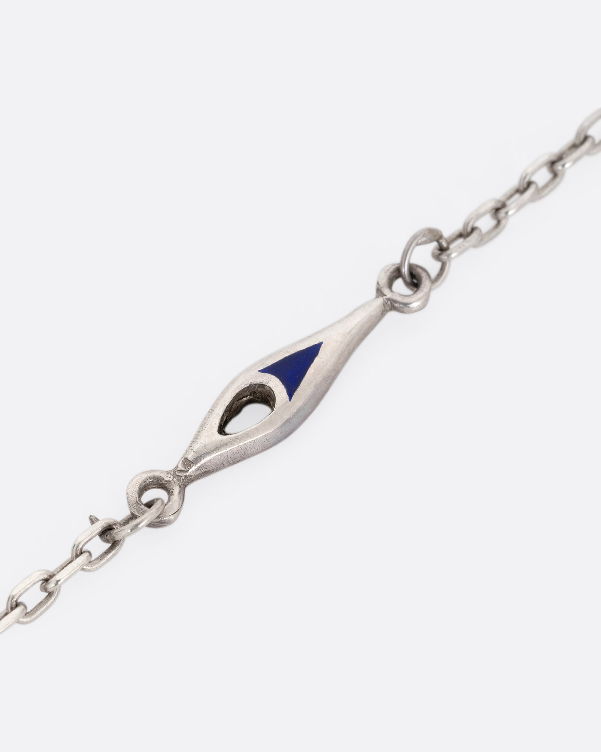A close up of a silver cable chain necklace with marquise shaped stations of blue enamel. 