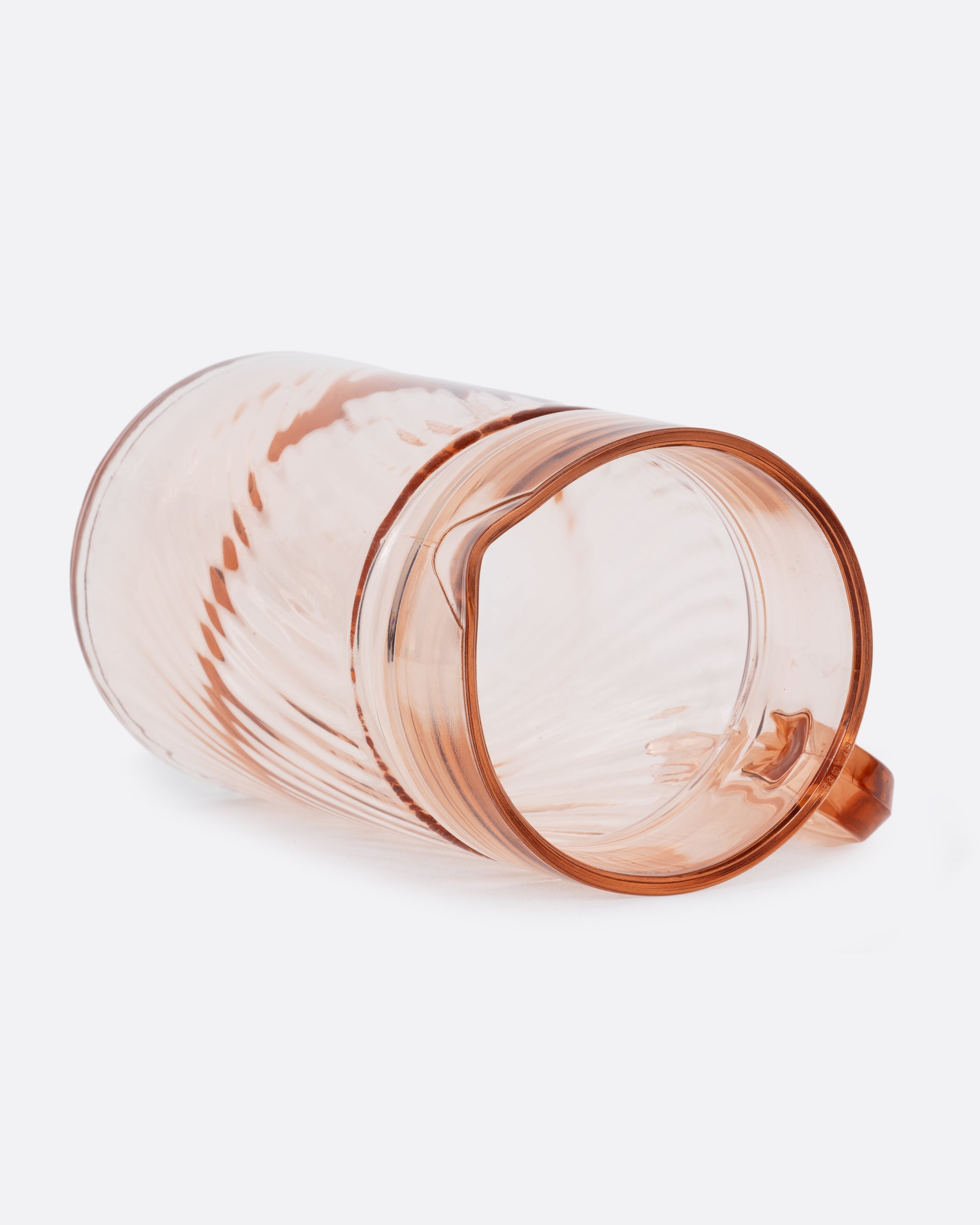 A pale pink glass pitcher with a twisted texture and sleek handle. Shown on it's side from the top.