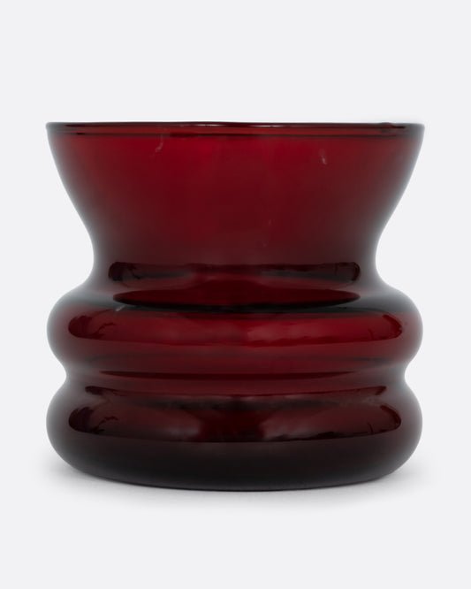 A short red glass vase with a wavy silhouette. Shown from the front.