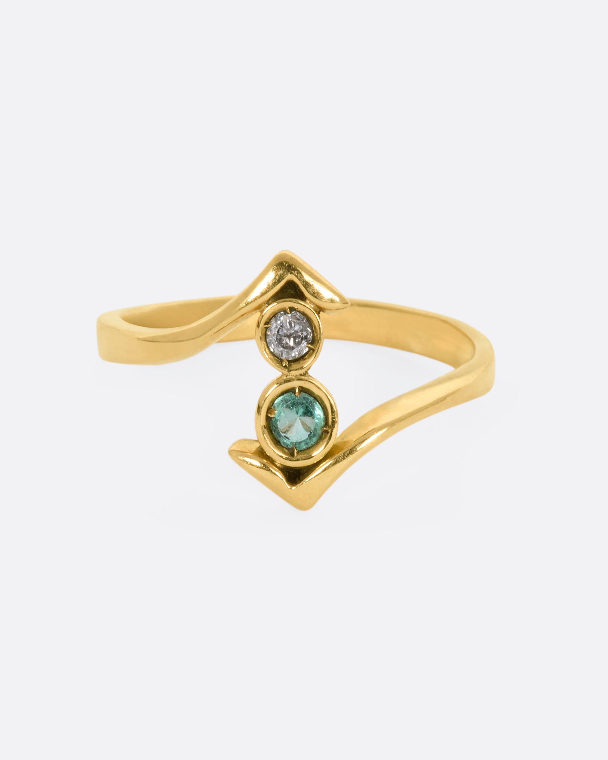 A yellow gold wrap ring with a round diamond and emerald. View from the front.