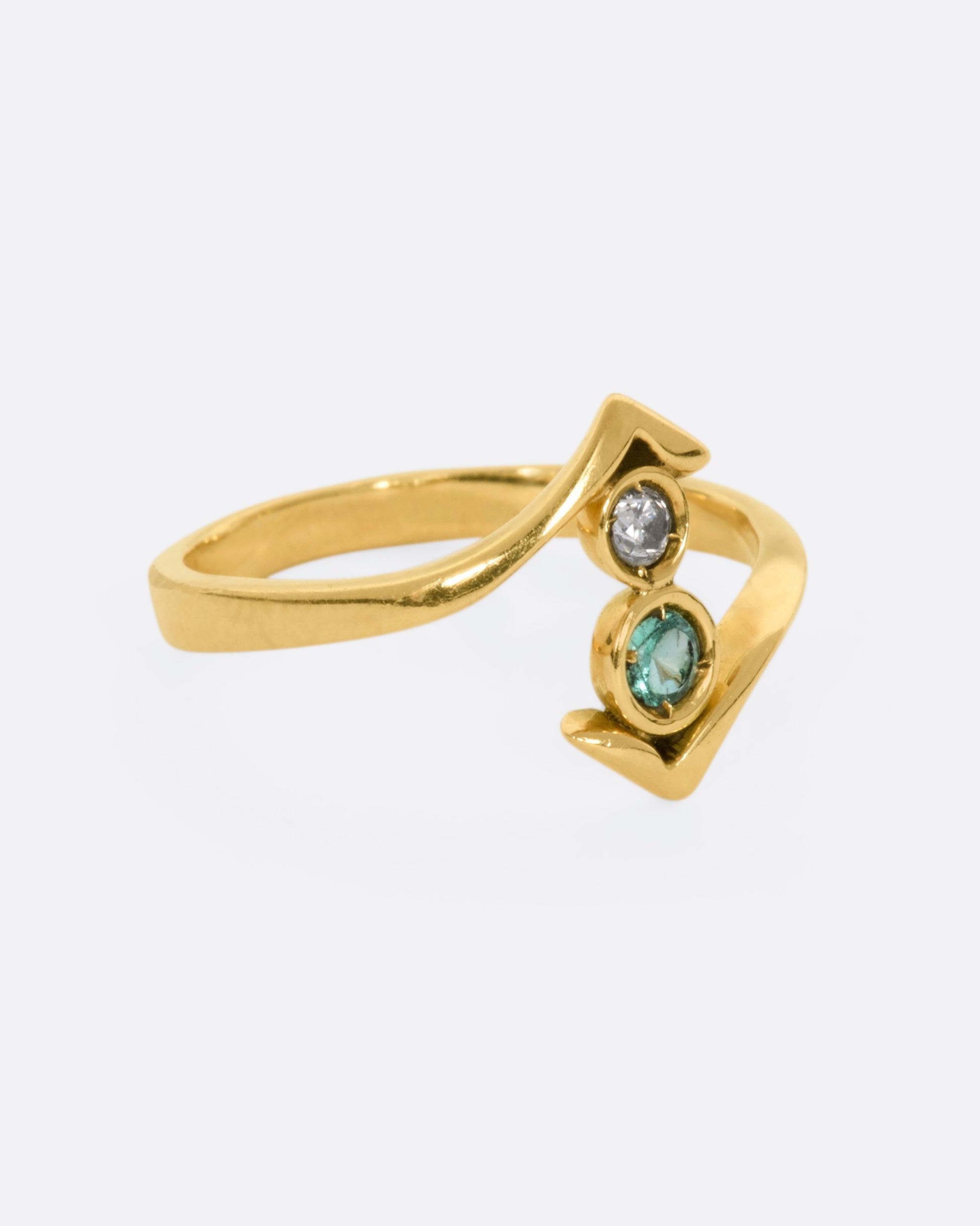 A yellow gold wrap ring with a round diamond and emerald. View from the side.