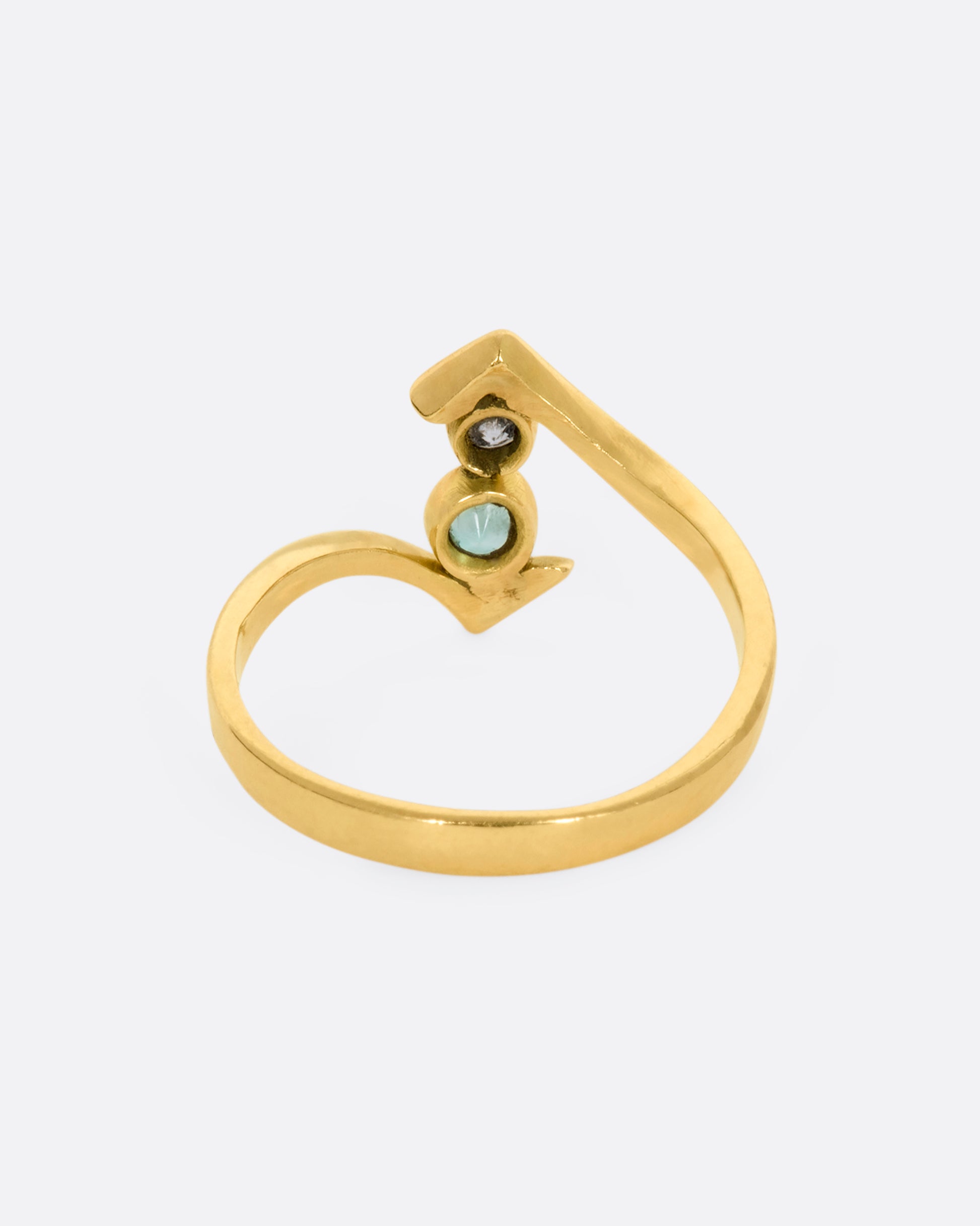 A yellow gold wrap ring with a round diamond and emerald. View from the back.