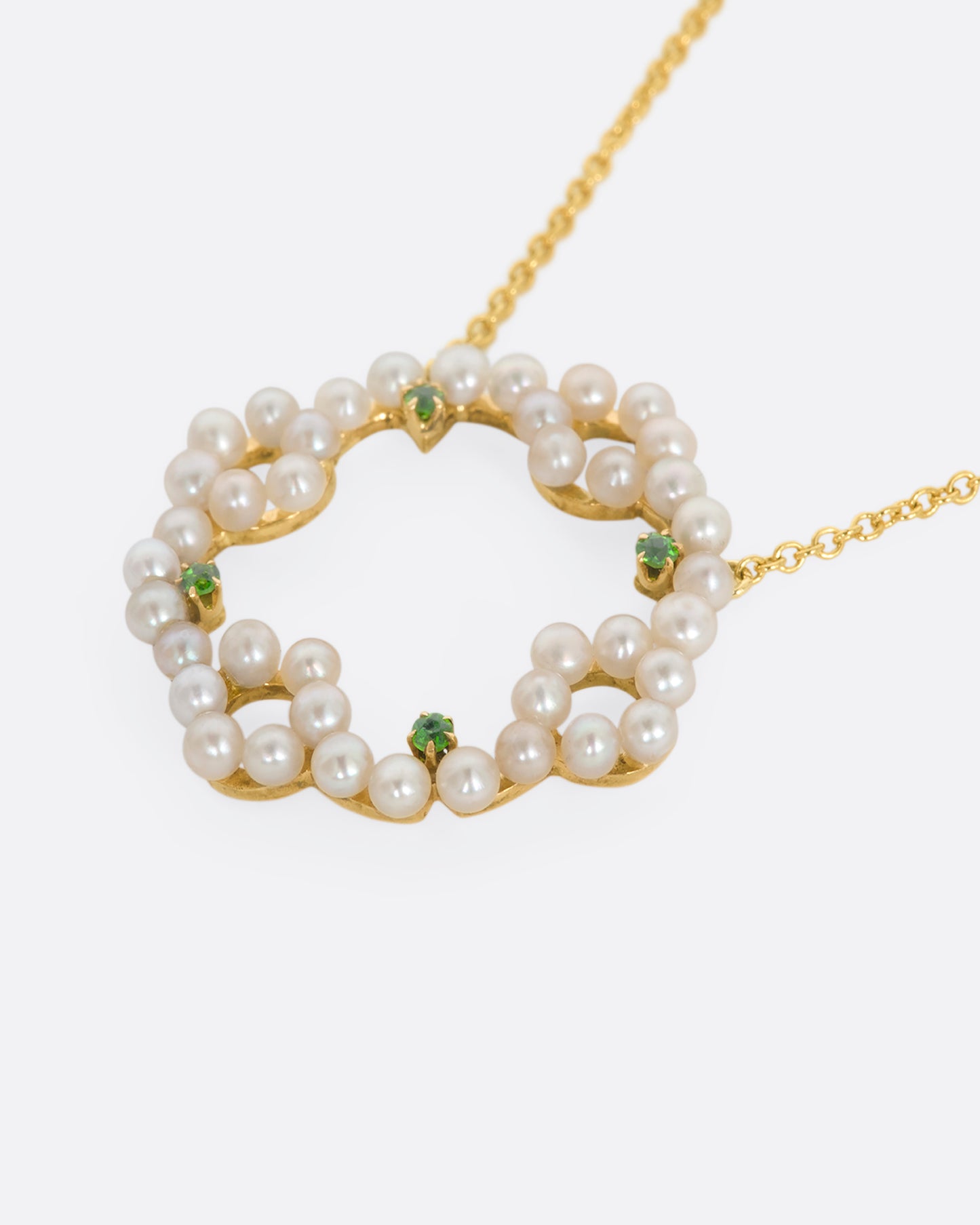 A yellow gold necklace with a pearl and green garnet wreath pendant. View laying flat.