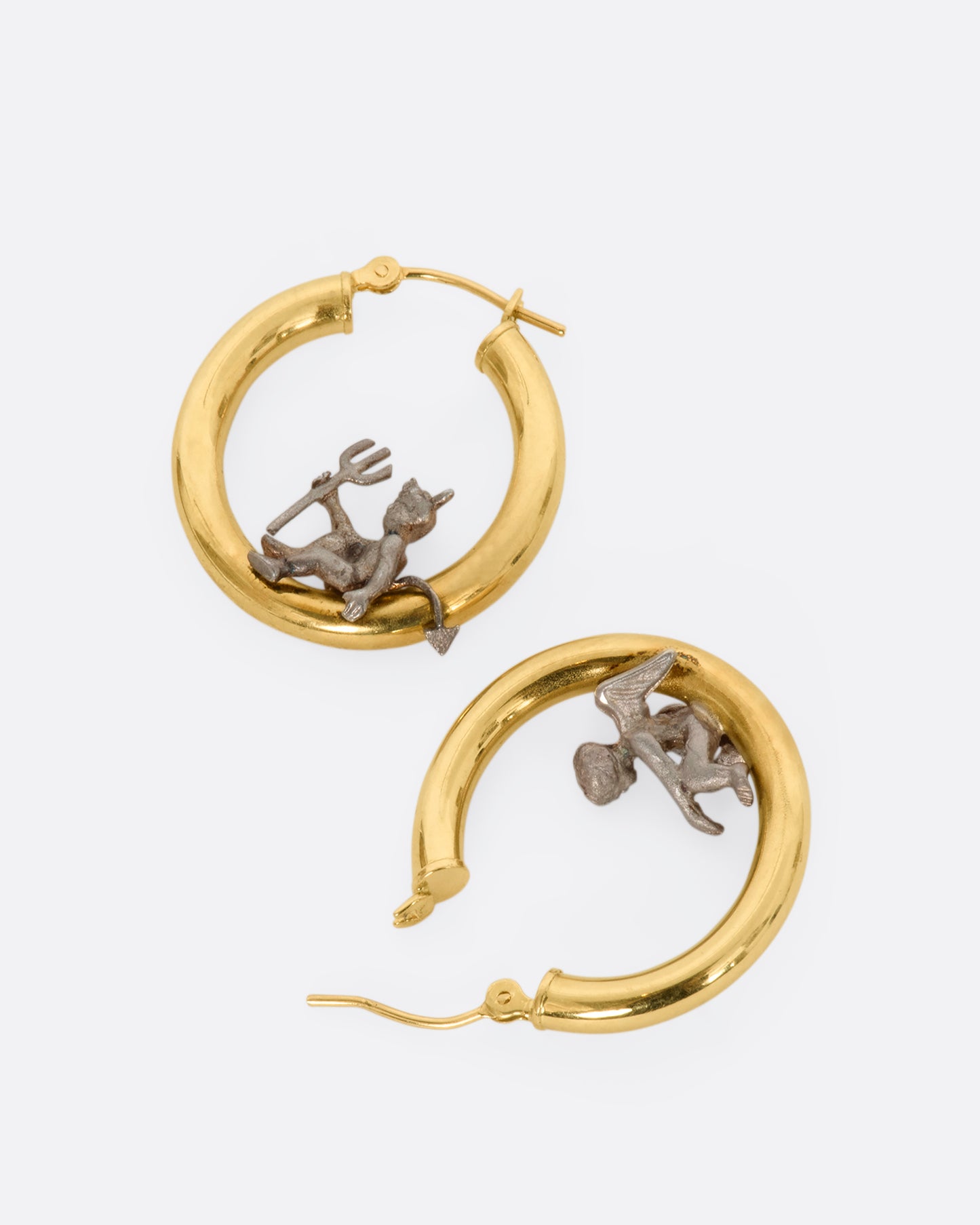 A pair of hoop earrings with an angel and devil perched on the inside. View laying flat.