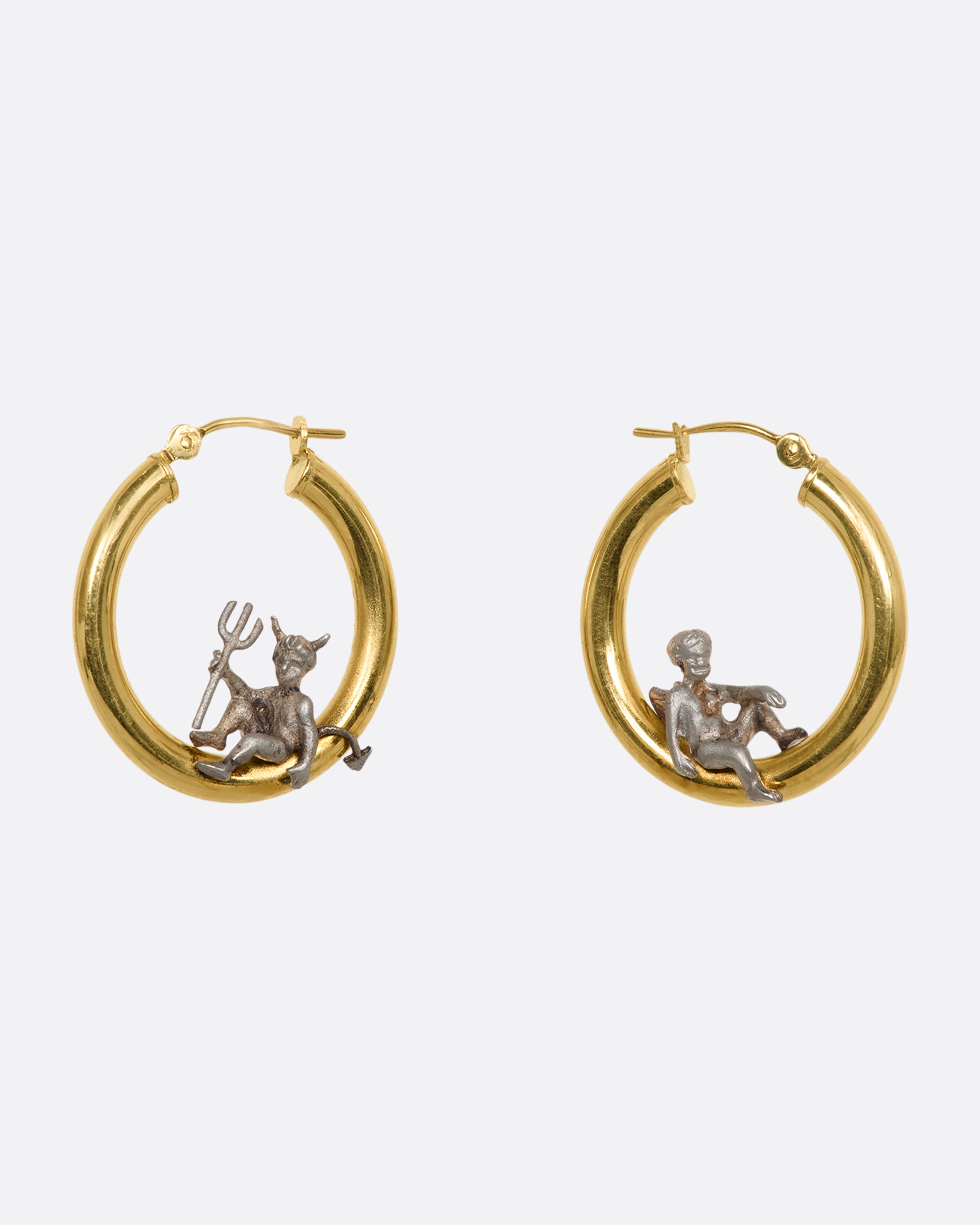 A pair of hoop earrings with an angel and devil perched on the inside. View from the side. 